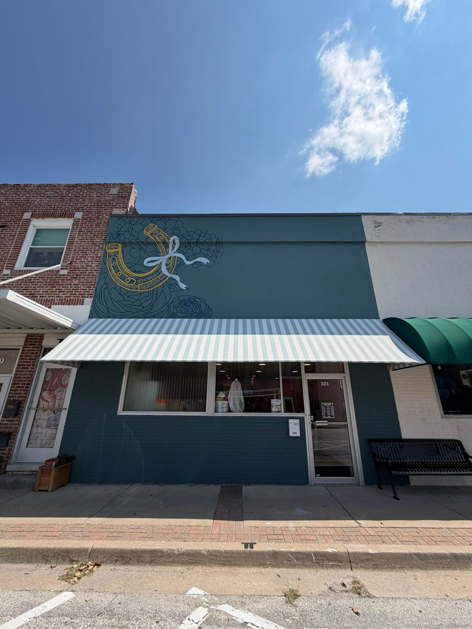 Building with a blue and gray exterior, glass door, and a green awning, under a partly cloudy sky.