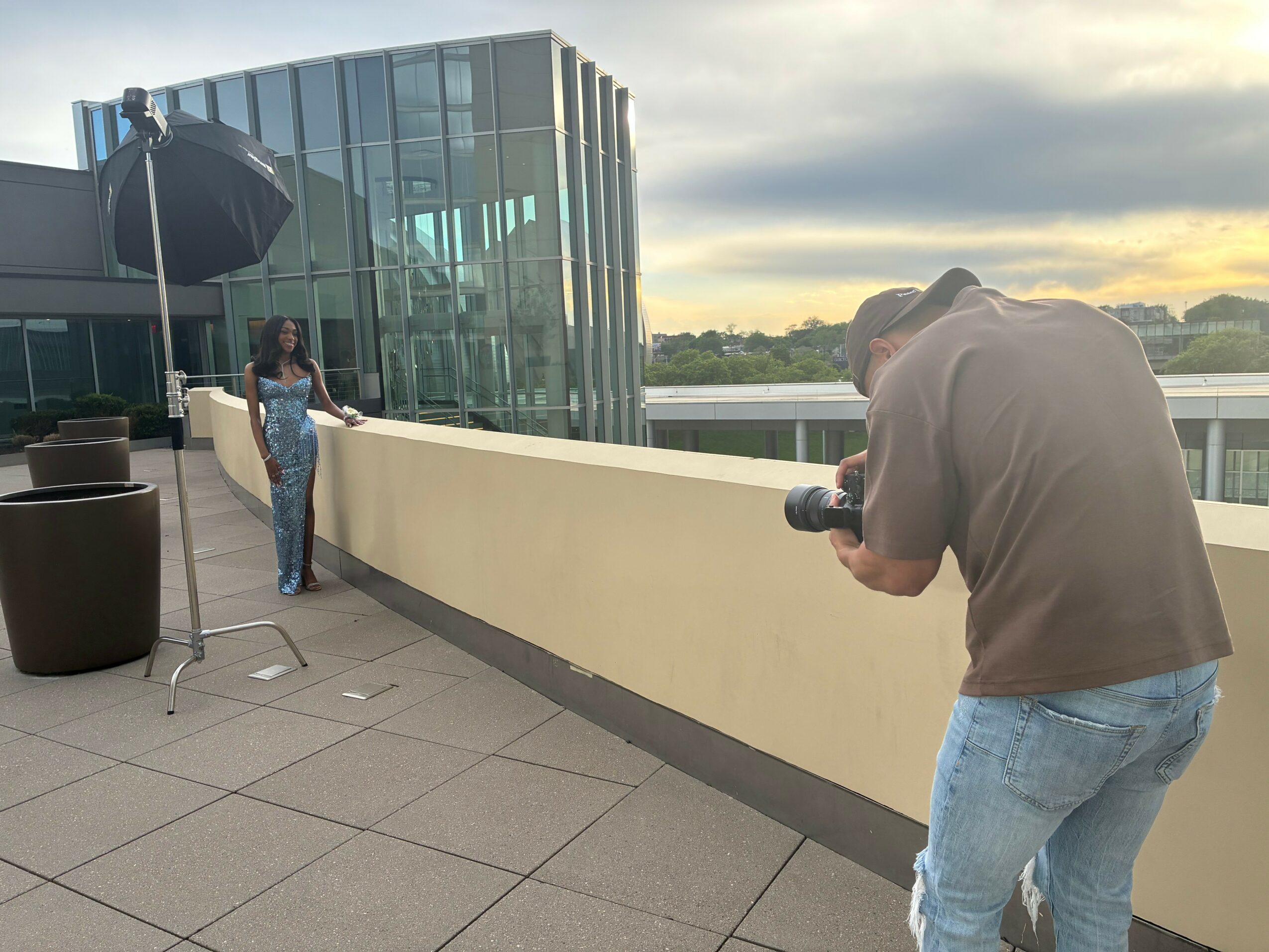 Photographer taking a picture of a woman on a rooftop terrace with a glass building in the background.