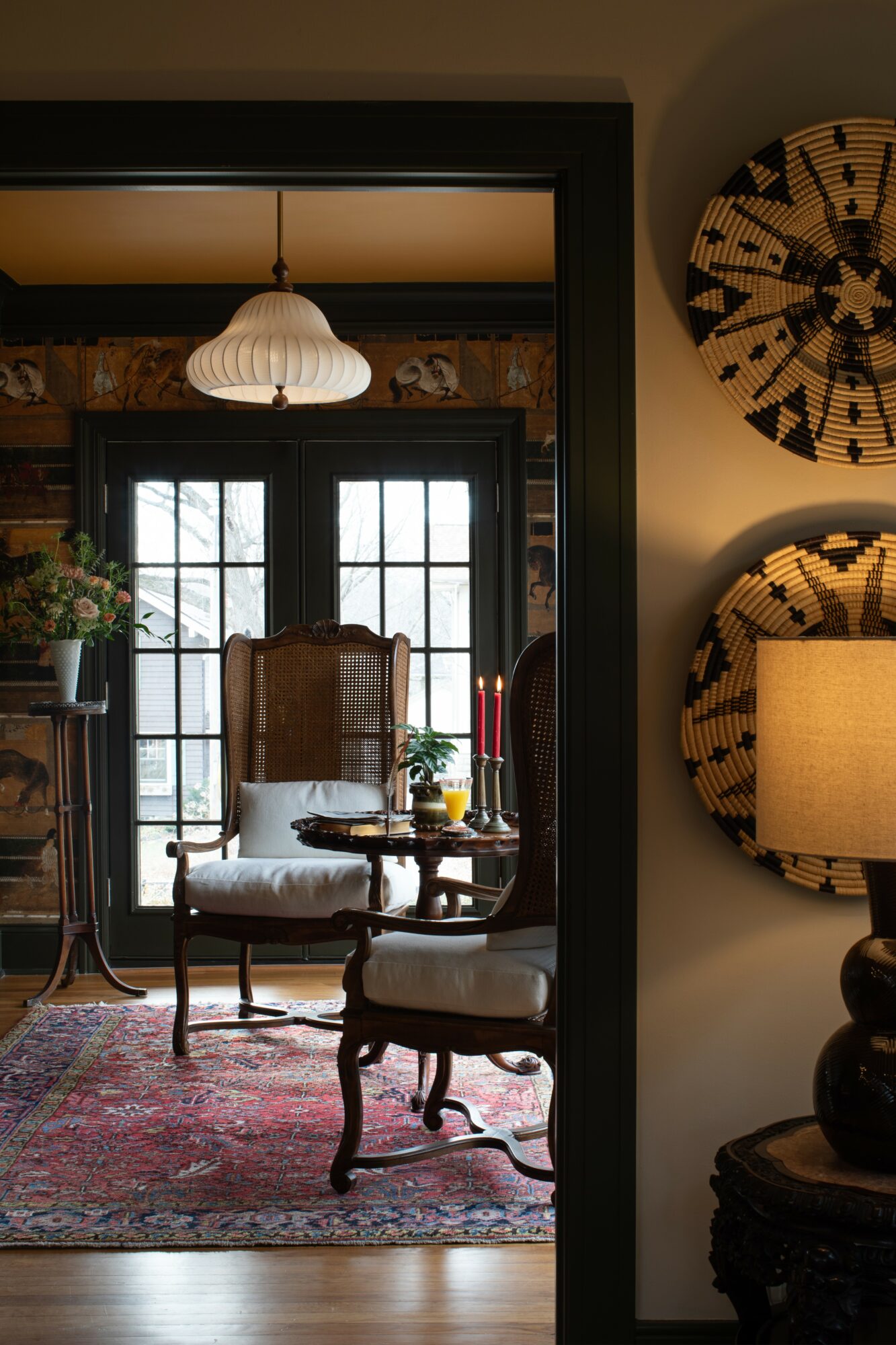 Interior view of a cozy room with a window seat, armchair, and a hanging lamp, seen through a doorway.