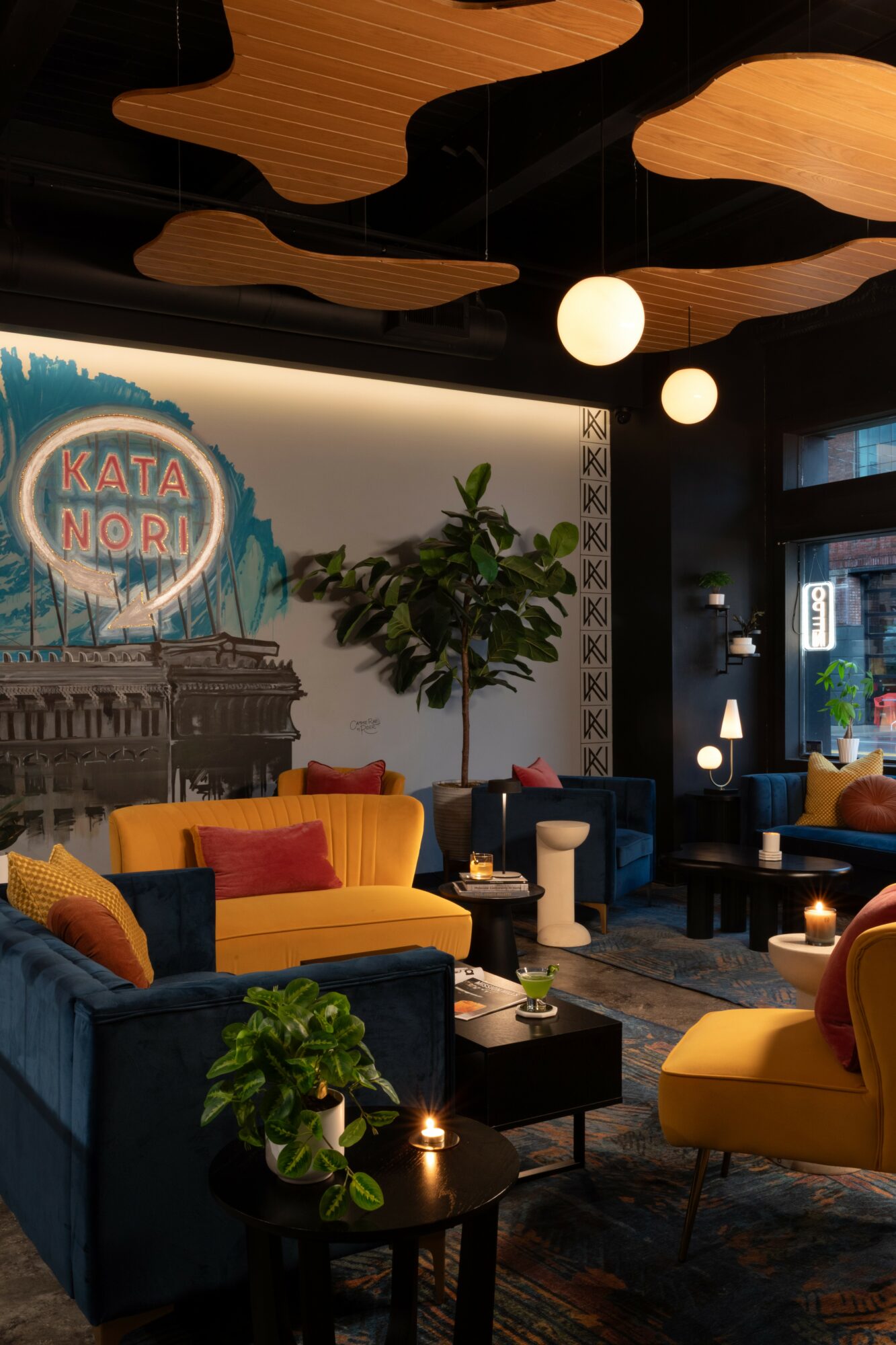 Interior of a lounge with colorful sofas, a large plant, and decorative ceiling elements, illuminated by hanging lights.
