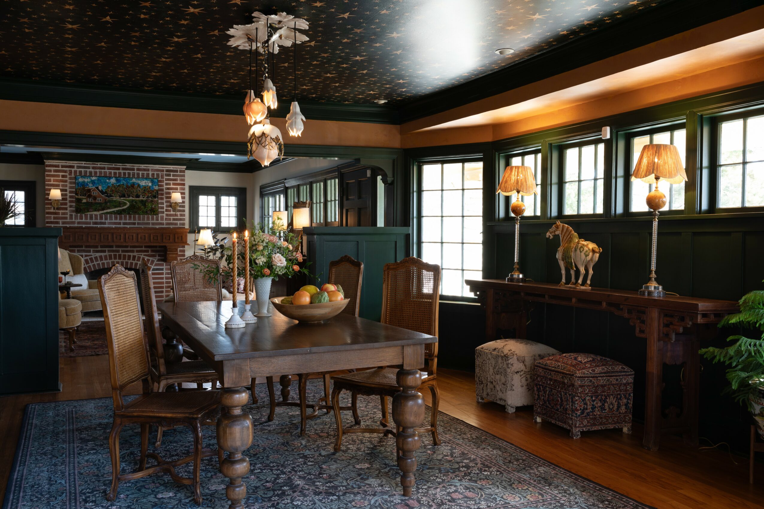 Elegant dining room with wooden table, chairs, large windows, and decorative lamps, featuring a dark ceiling and wooden flooring.