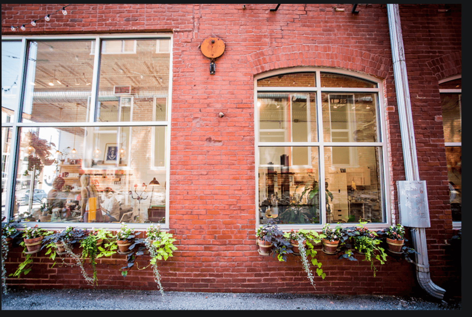 Red brick building with large windows and flower boxes, reflecting interior and exterior scenes.