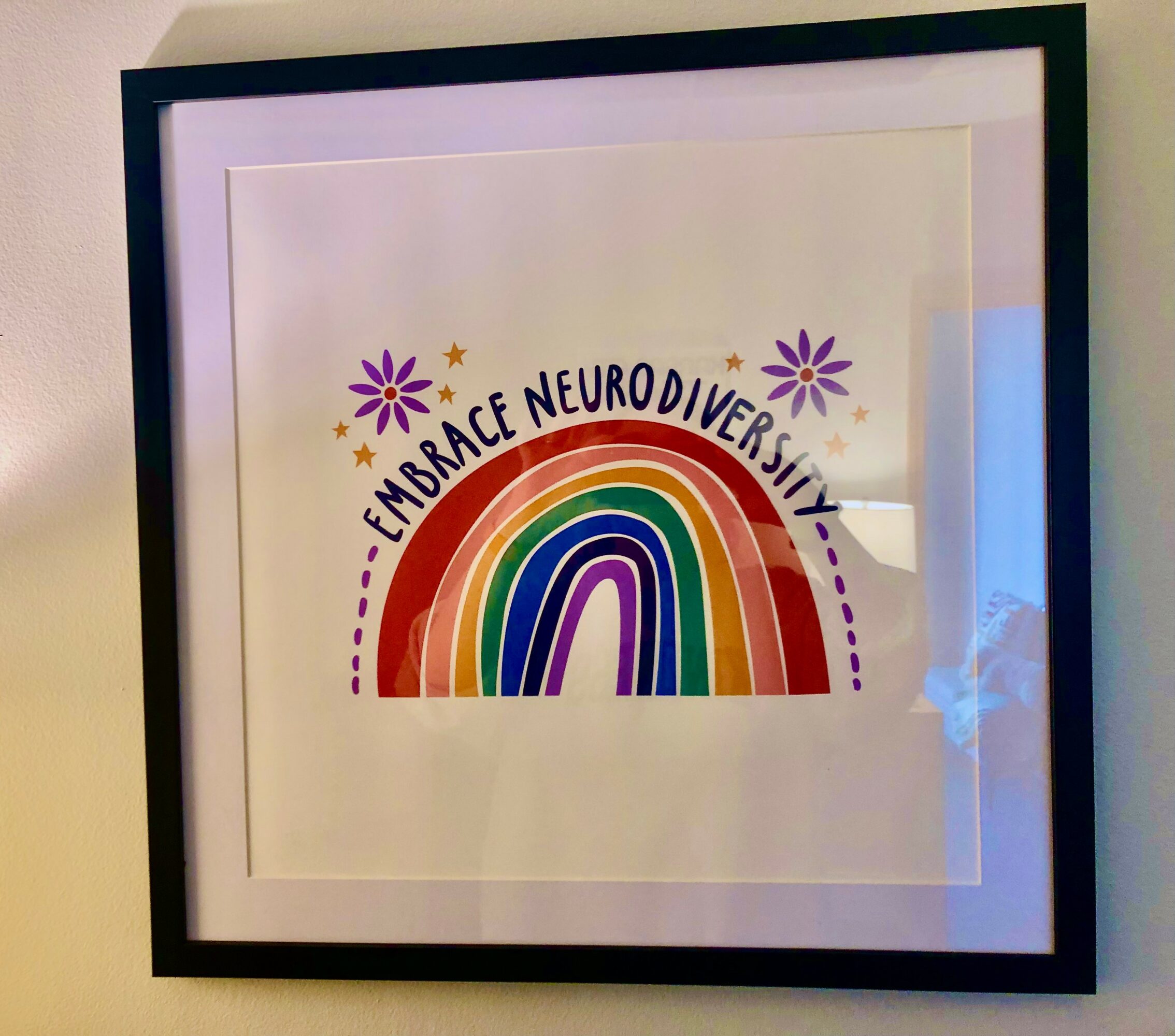 Framed artwork with a rainbow, purple flowers, and the text 'Embrace Neurodiversity' above the rainbow.