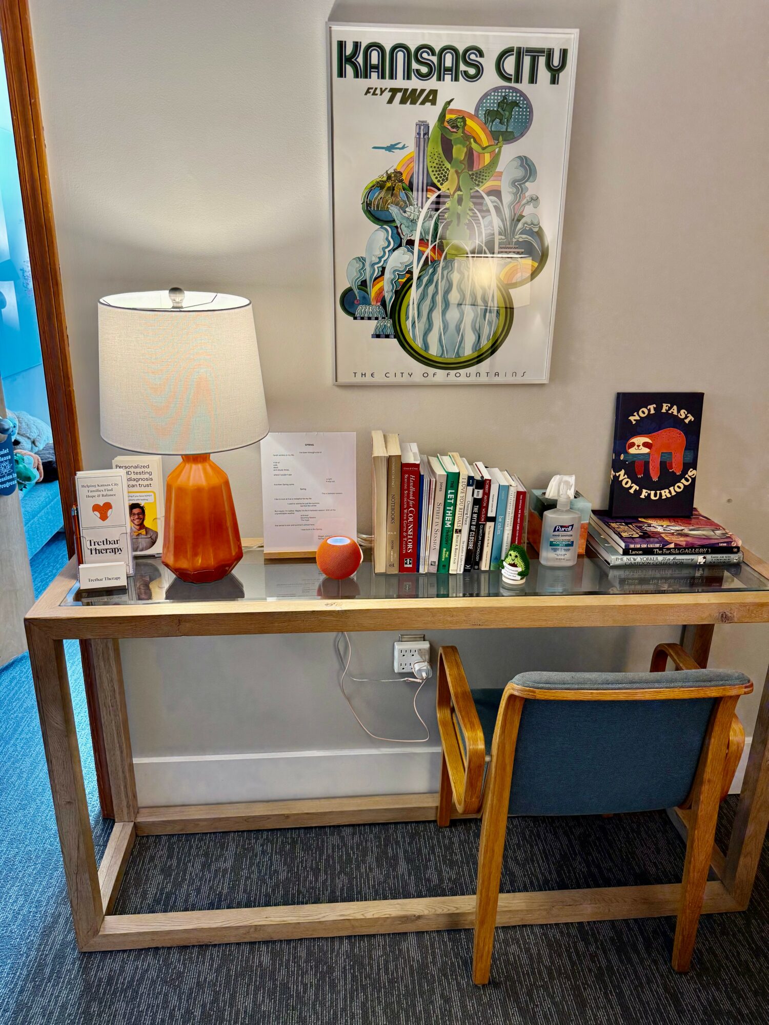 Desk with lamp, books, and decorations, and a chair in front, against a wall with a Kansas City poster.
