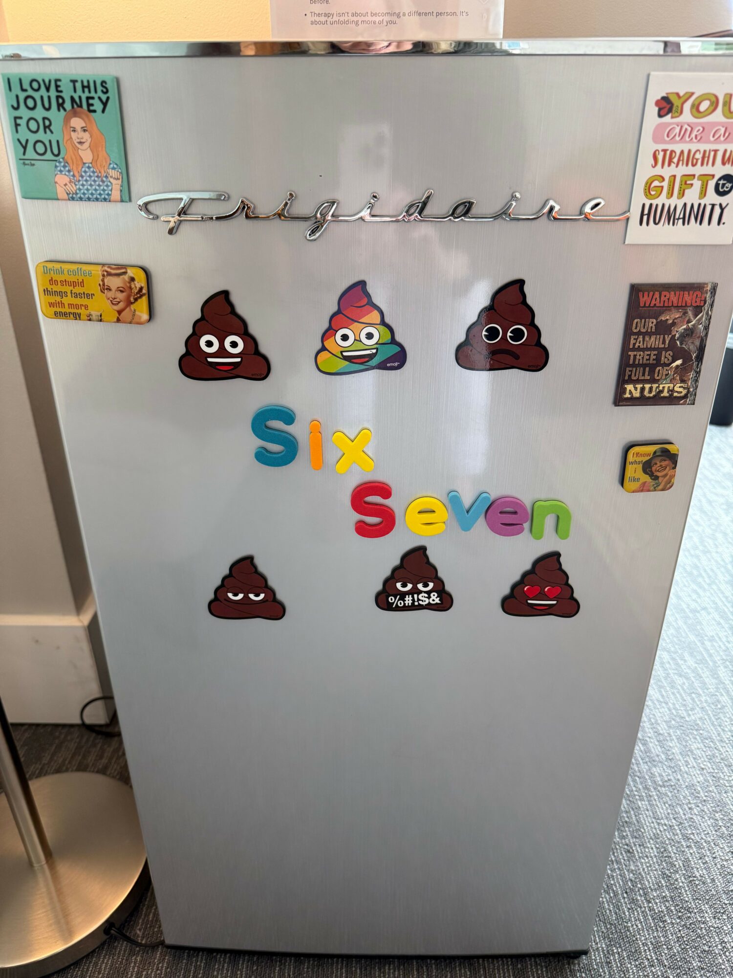 A refrigerator door with colorful stickers, including a six-pack of poop emojis, and the words 'Six Sevu' in colorful letters.