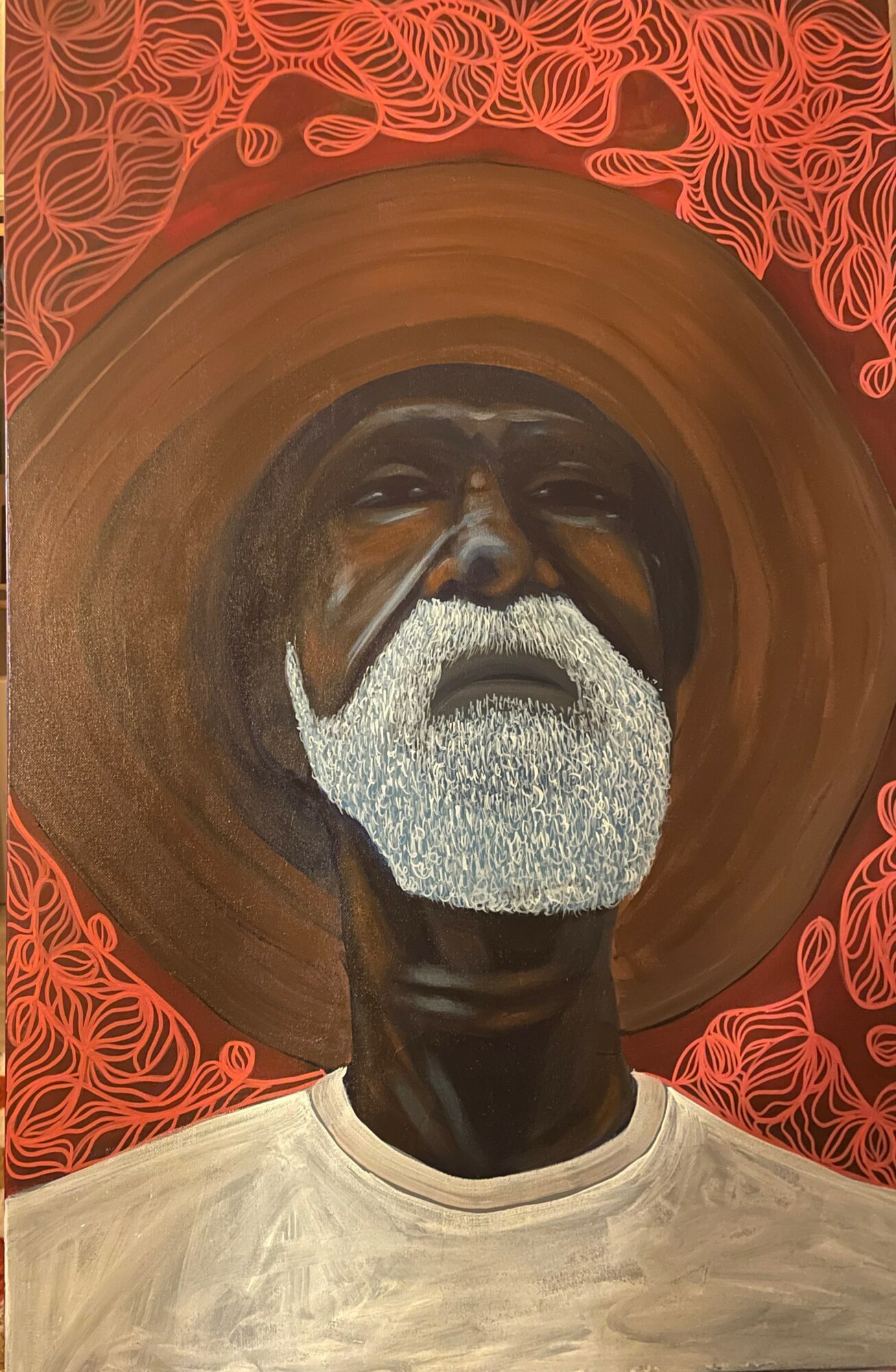Portrait of an elderly man with a white beard wearing a large straw hat, against a red patterned background.