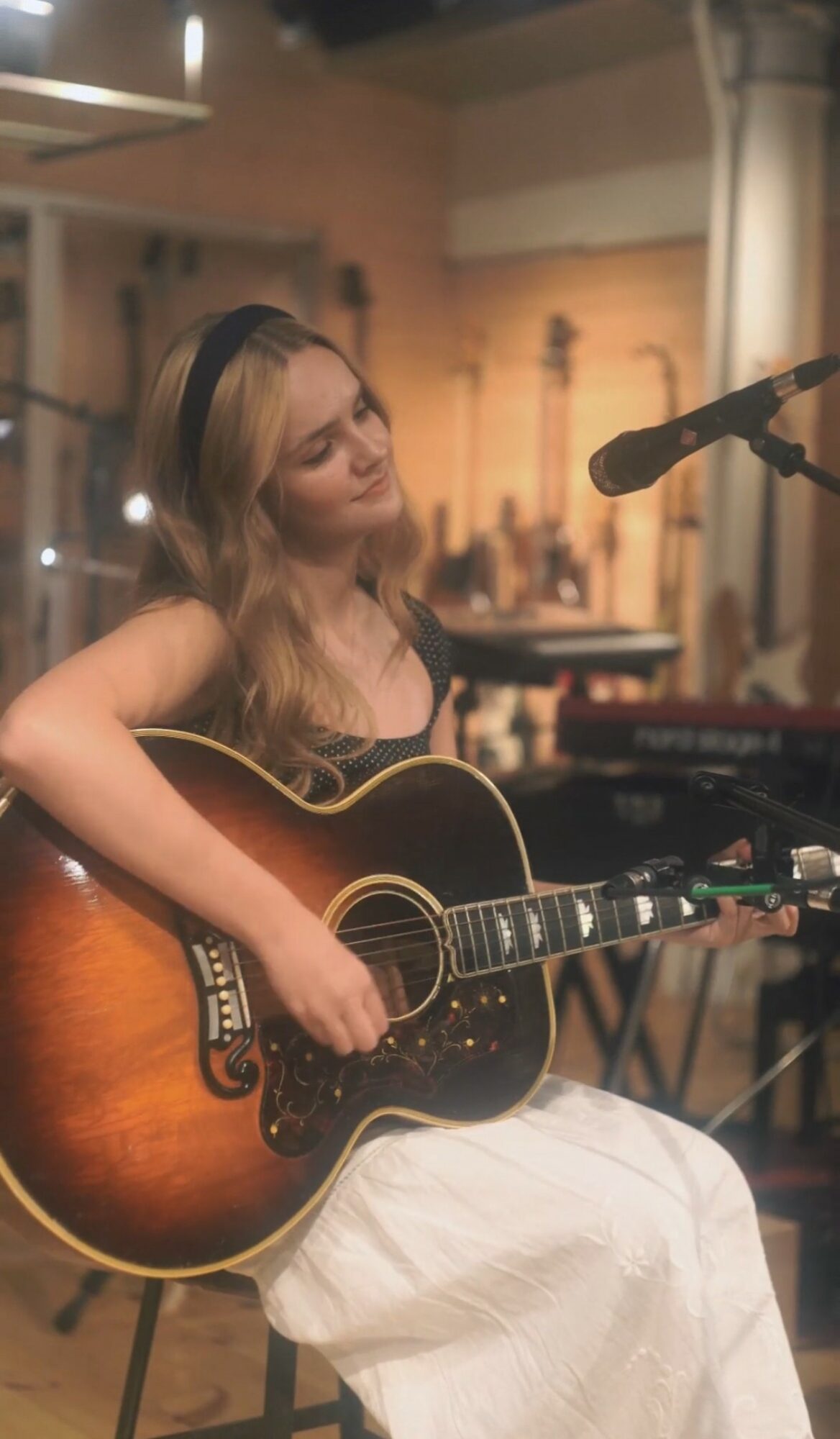 Woman playing an acoustic guitar in a recording studio with a microphone nearby.