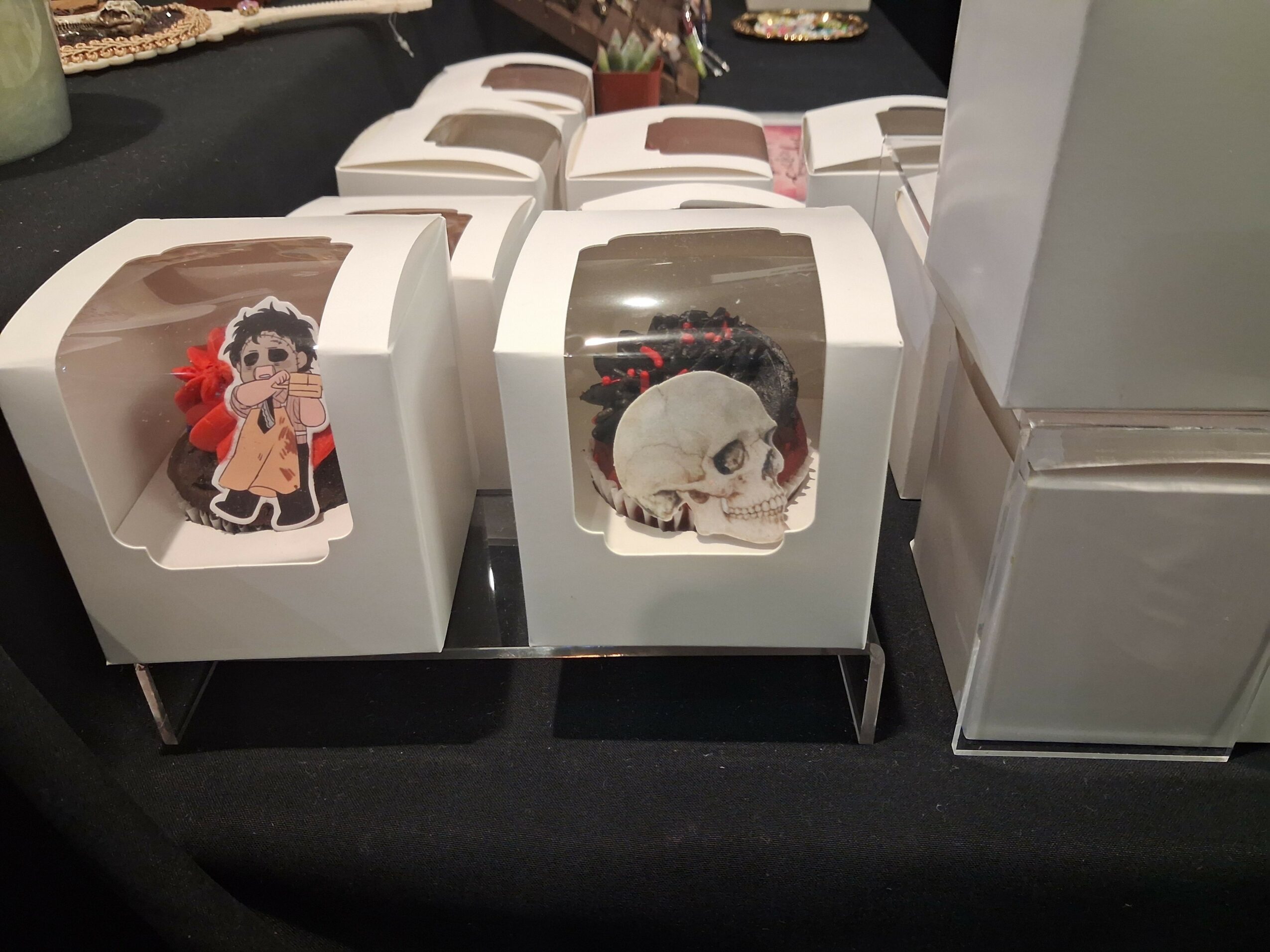 Boxes with clear plastic windows displaying cartoon stickers of a girl and a skull, on a black surface.