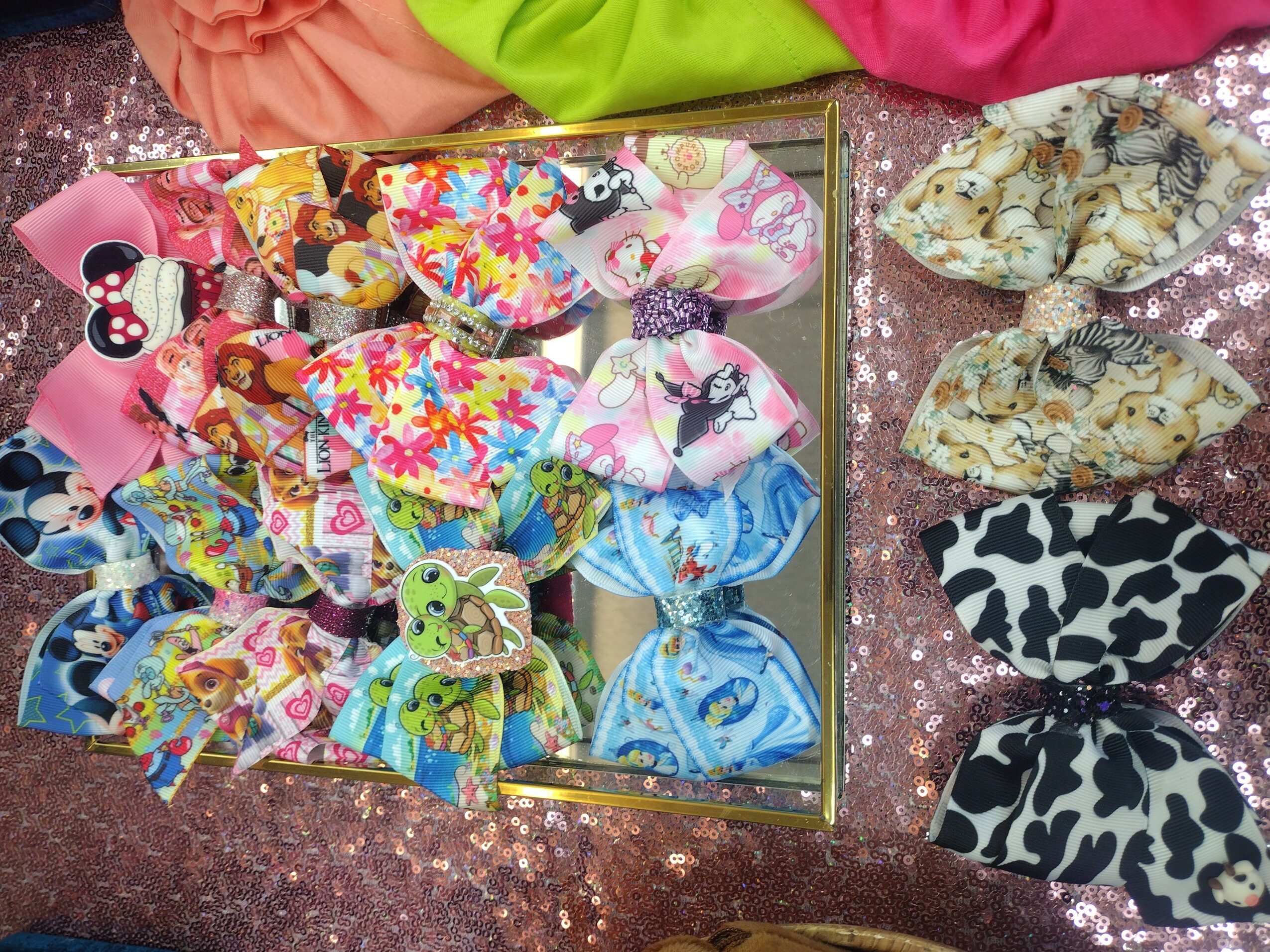 Collection of colorful fabric hair scrunchies and headbands with various patterns, some with cartoon characters, on a glittery surface.