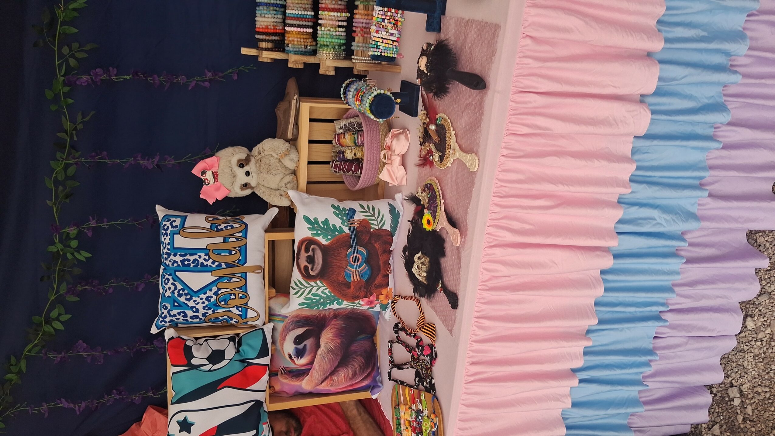 Display of colorful toys and decorations on a pink and blue ruffled tablecloth, with a dark background and greenery.