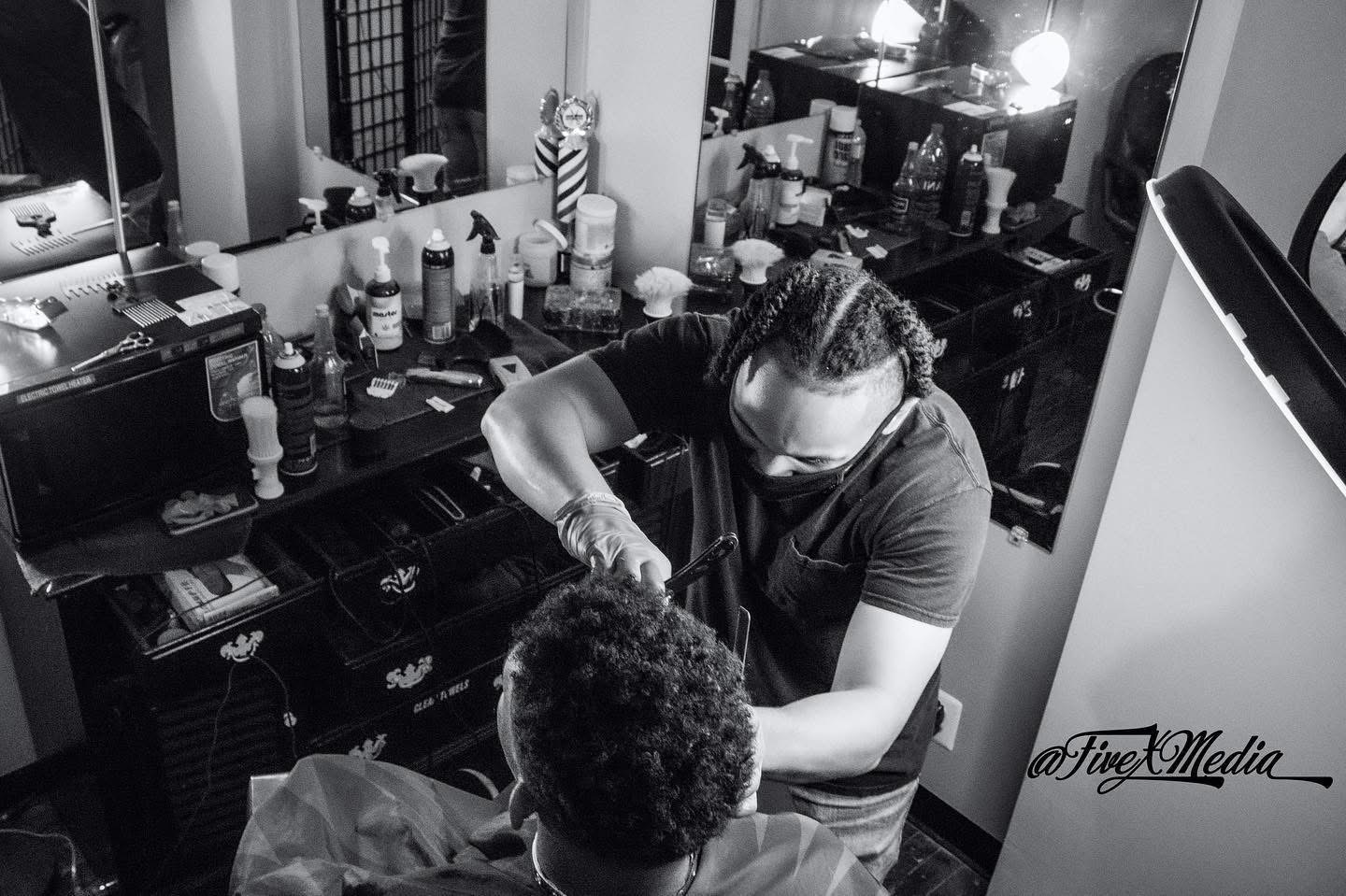 A person with braided hair applies makeup to a seated individual in a room with makeup products on a counter.