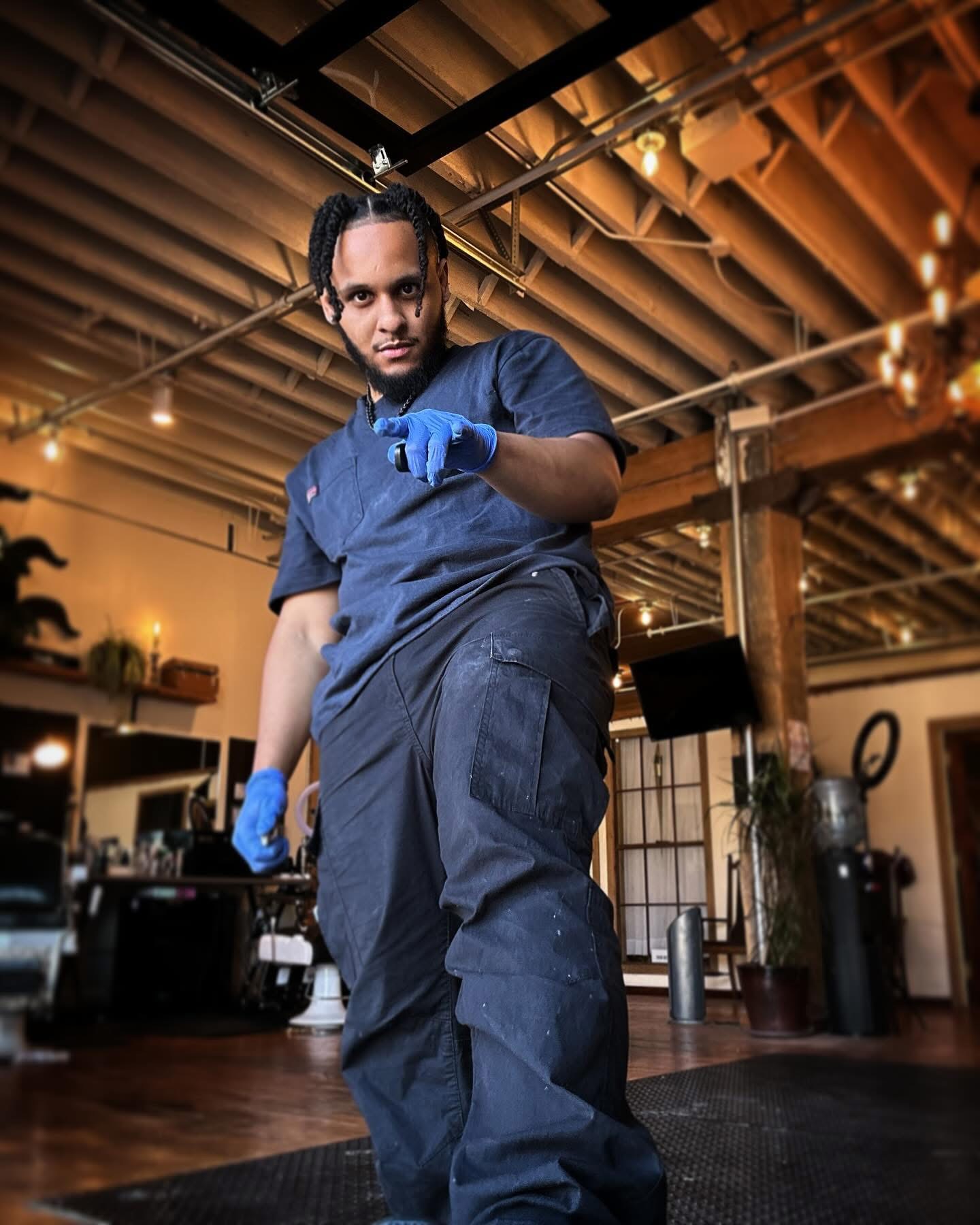 Person in dark clothing and blue gloves pointing forward in an industrial-style room with warm lighting.
