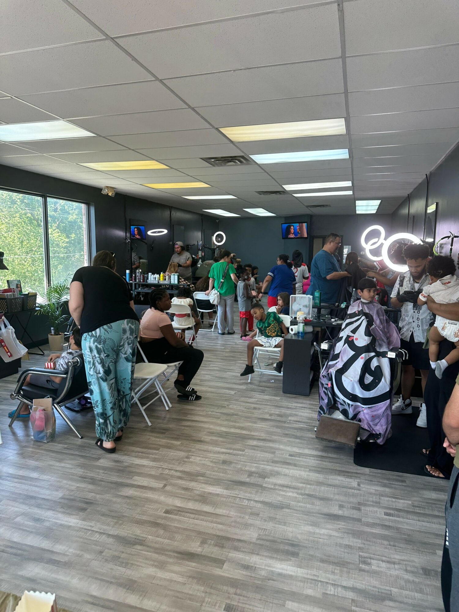 People waiting in line at an airport check-in counter, with some sitting on luggage, in a modern terminal.
