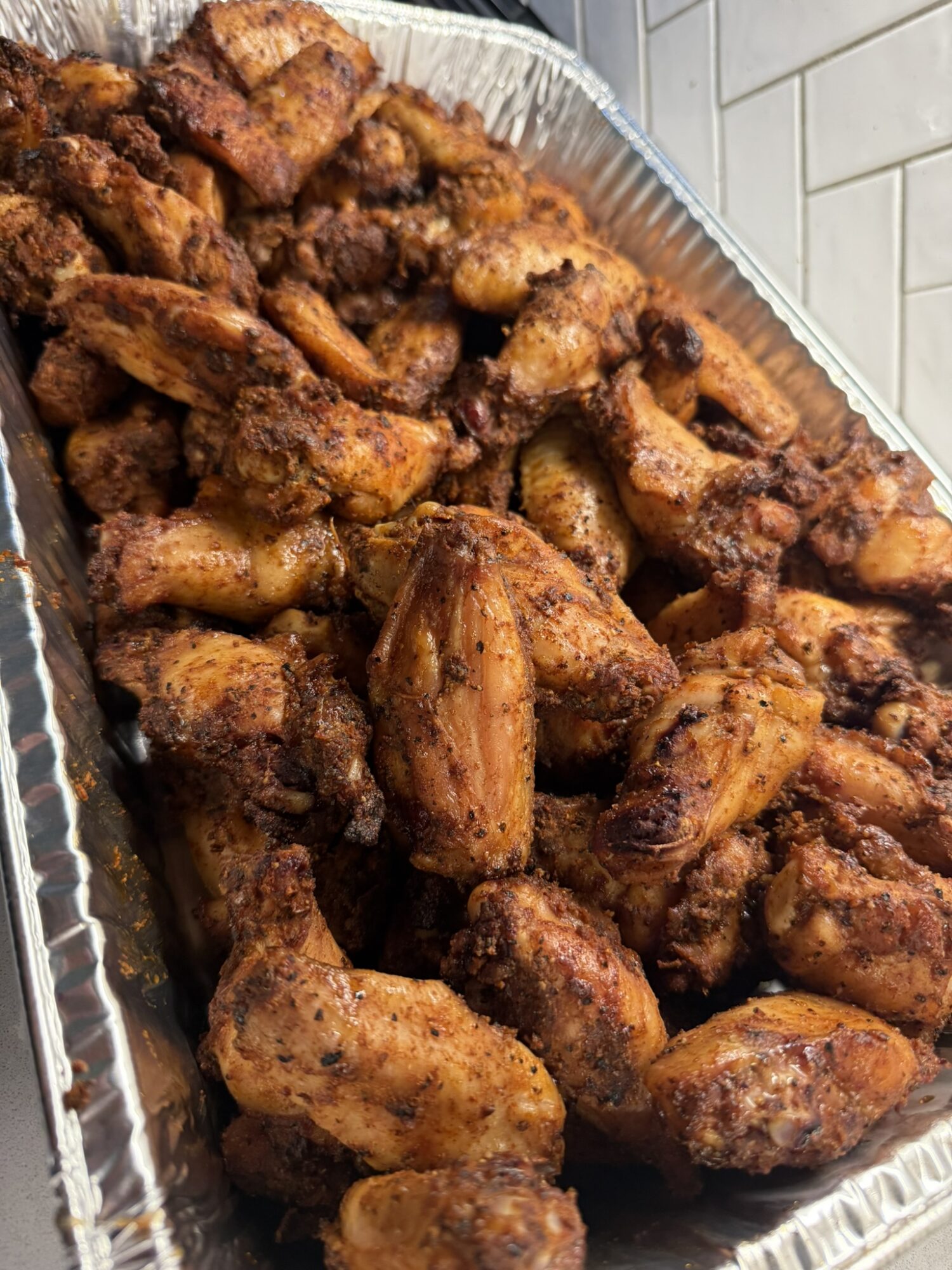 Tray filled with cooked, crispy chicken wings and drumsticks, placed on a tiled surface.