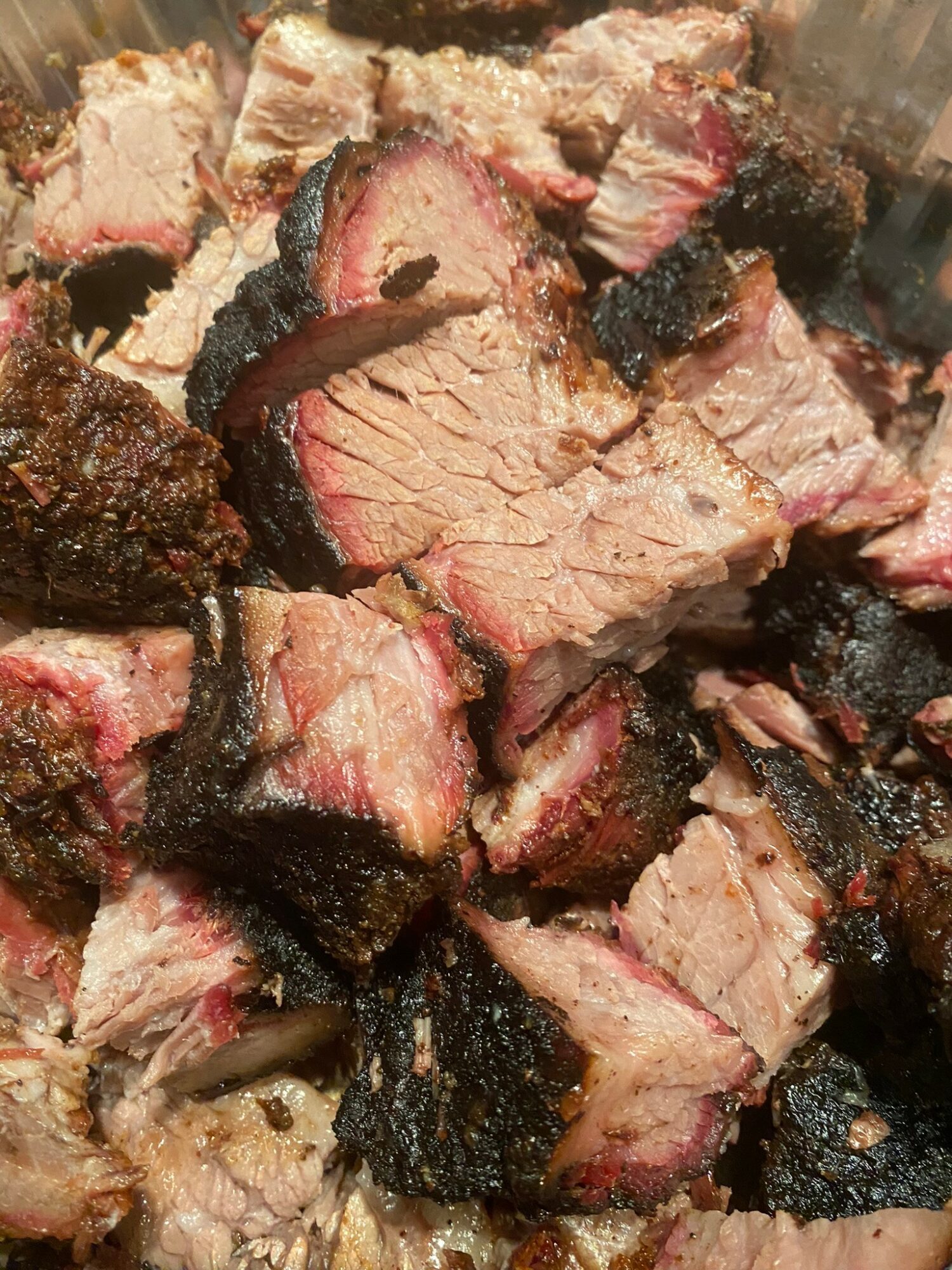 Pieces of cooked meat with a charred exterior and pink interior, some with visible fat, in a close-up view.