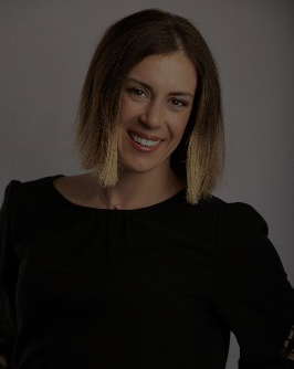 Smiling woman with shoulder-length hair wearing a black top against a plain background.
