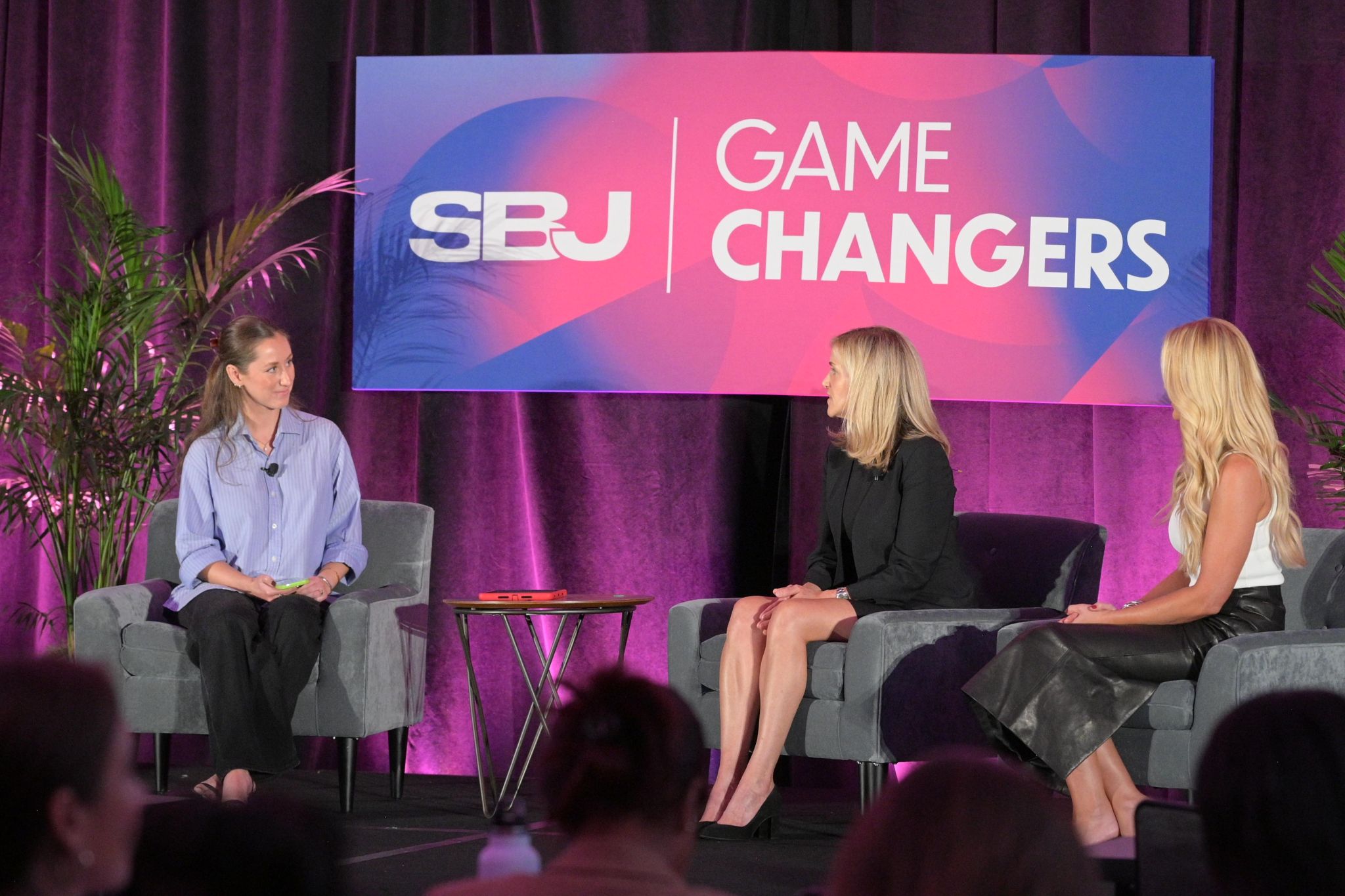 Three women seated on stage in front of a large screen with text, during a panel discussion.