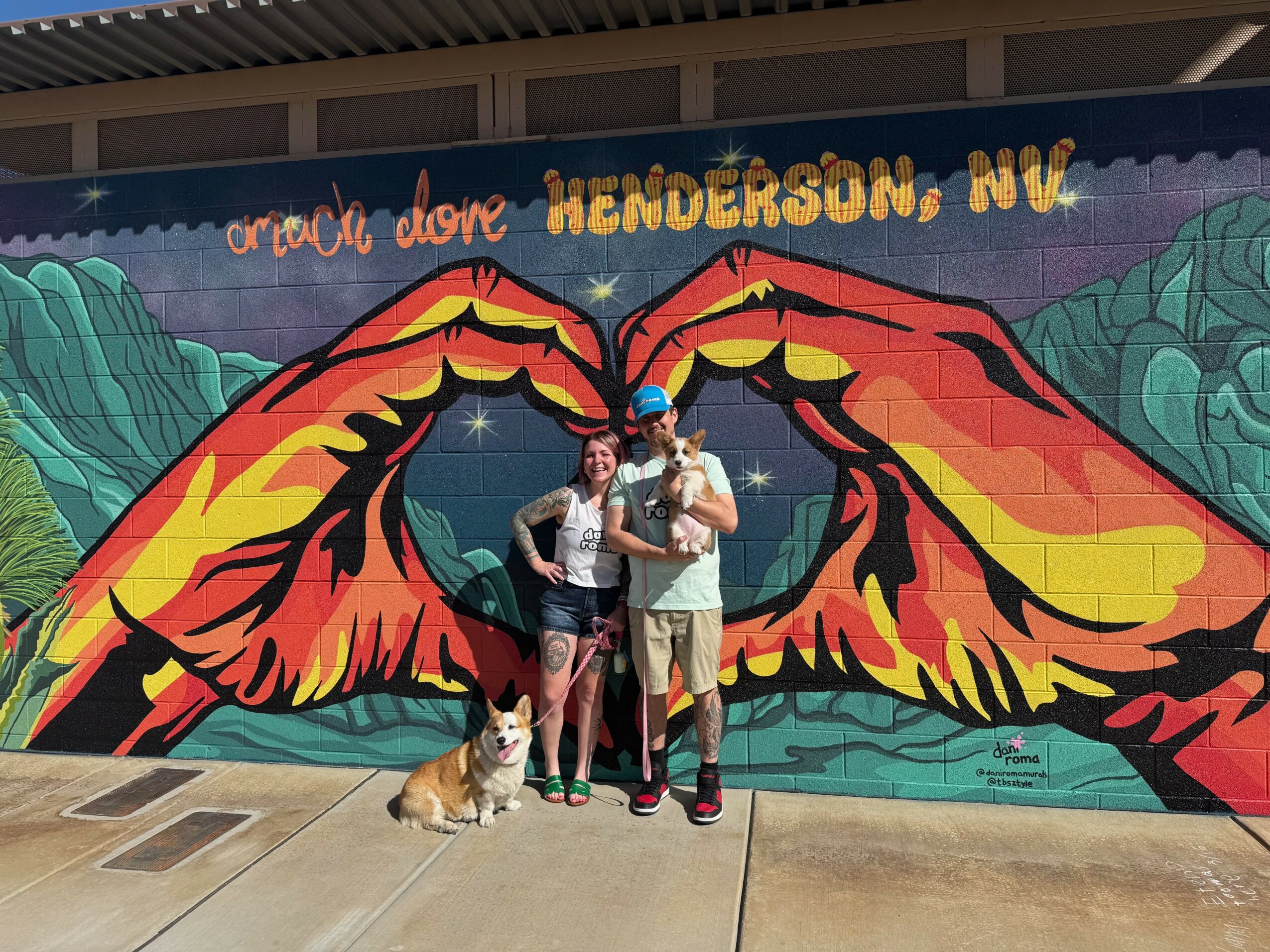 Three people and a dog stand in front of a colorful mural with large butterfly wings, Henderson, Nevada, visible text.