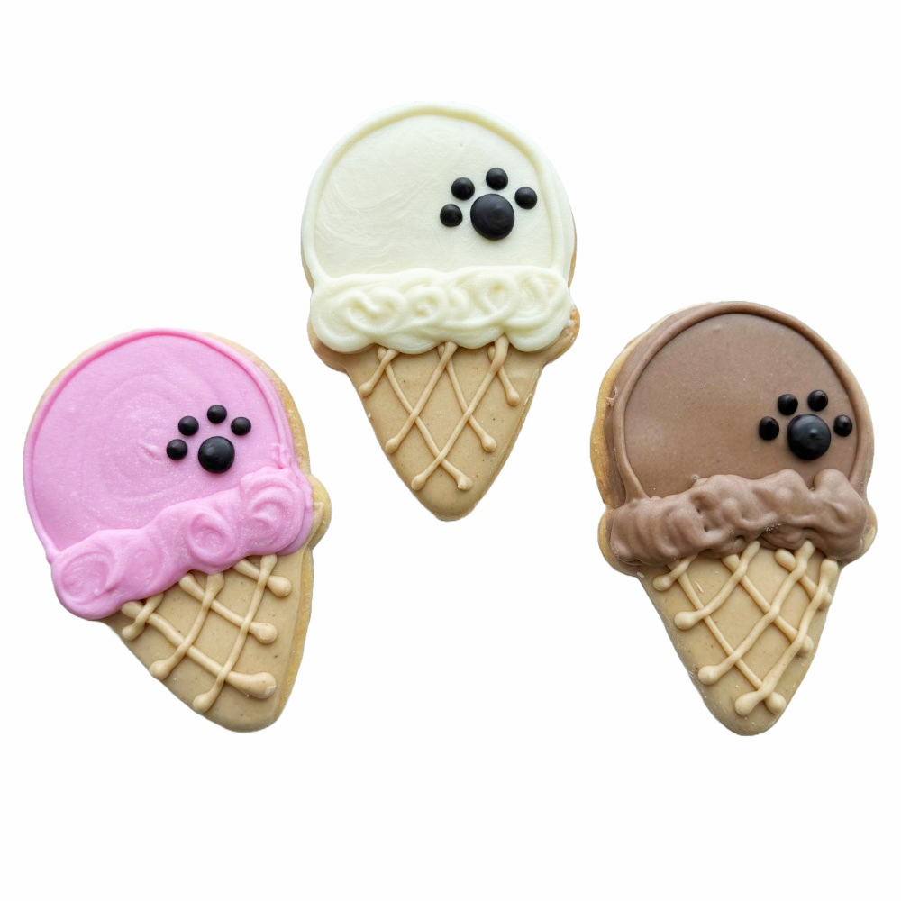 Three ice cream cone cookies with different colored frosting: white, pink, and brown, each with black candy eyes and a nose.