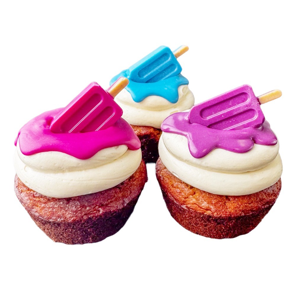 Three cupcakes with colorful popsicles on top, pink, blue, and purple, against a white background.