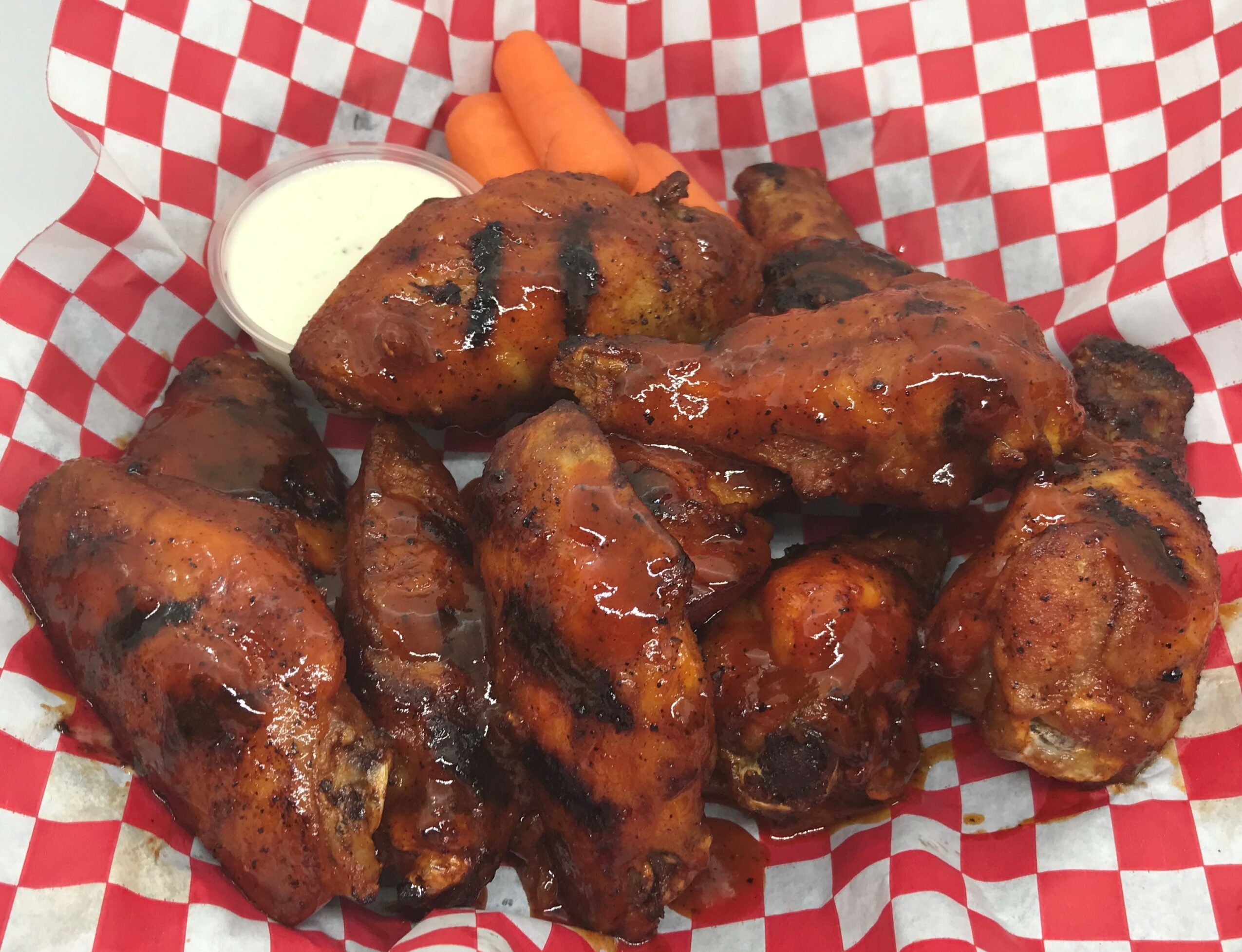 Plate of glazed chicken wings with dipping sauce and carrots on checkered paper