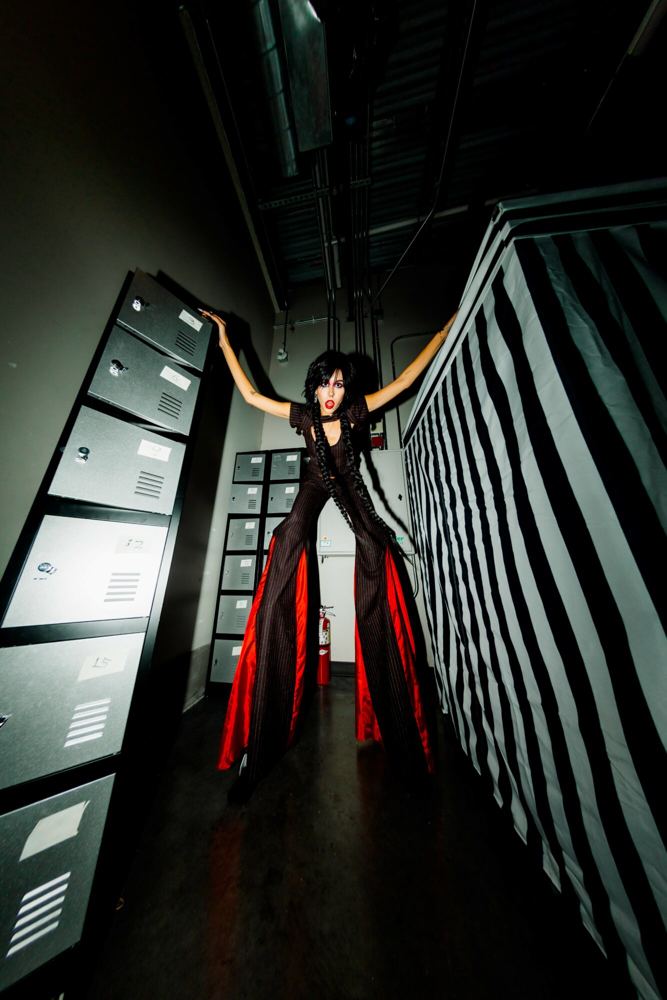 Person with arms outstretched standing between lockers and a striped wall in a dark room.