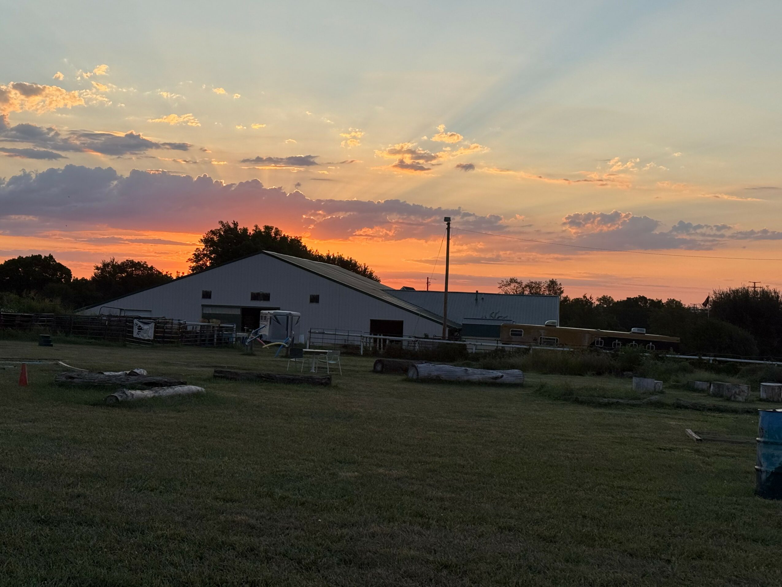 Farm buildings and open field at sunset with colorful sky and clouds.