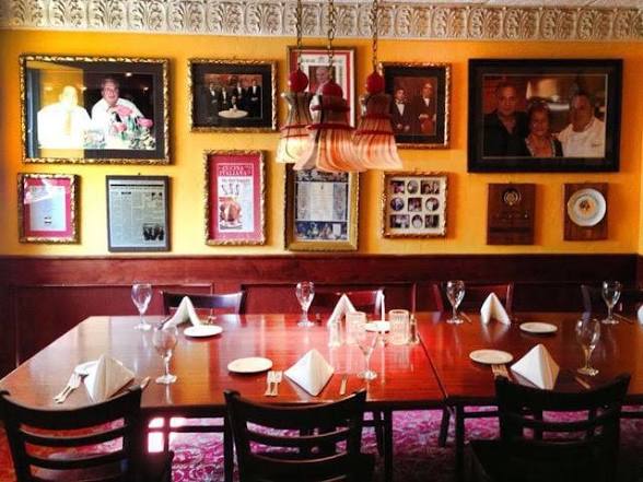 Dining room with a table set for six, framed photos on the wall, and a hanging lamp, in a cozy restaurant.