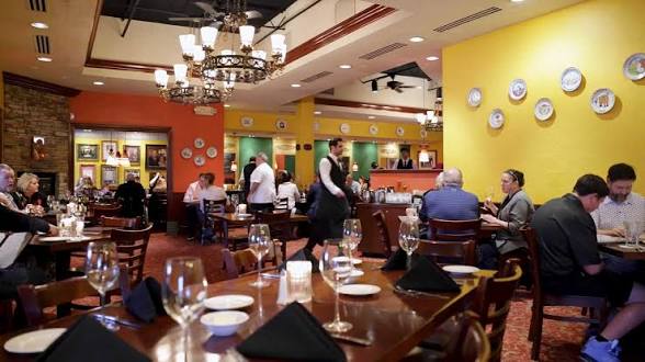 Restaurant interior with tables, chairs, and diners, colorful walls, and decorative plates on a yellow wall.