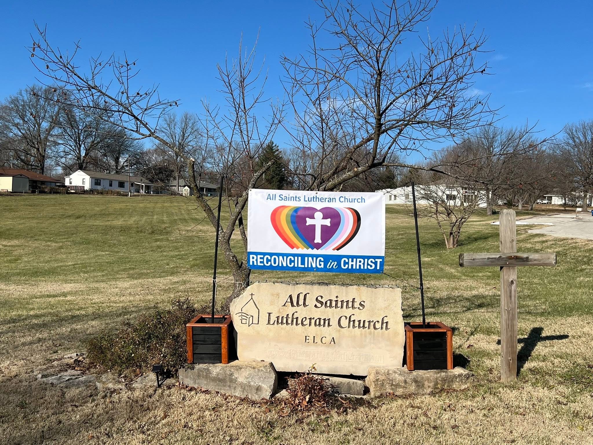 Sign for All Saints Lutheran Church and ELCA, with trees and a grassy area in the background.