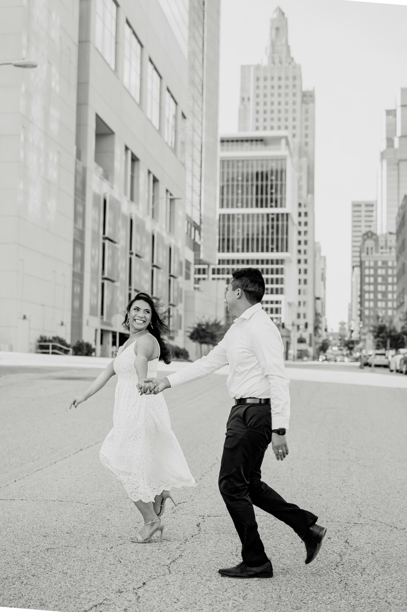 A couple dancing in a city street with tall buildings in the background, holding hands and smiling.