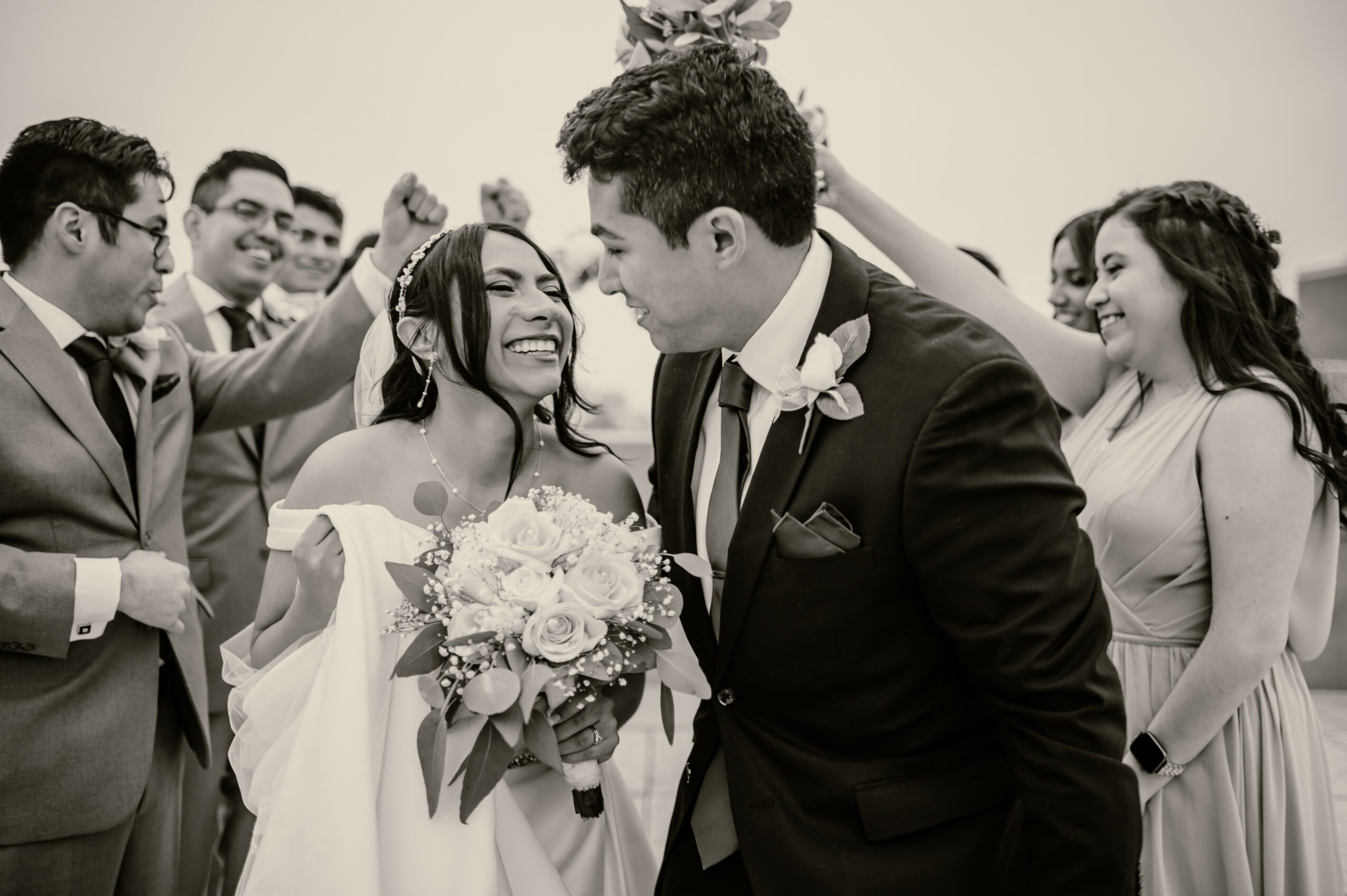 Group of people celebrating wedding, with bride holding bouquet and groom smiling, in black and white.