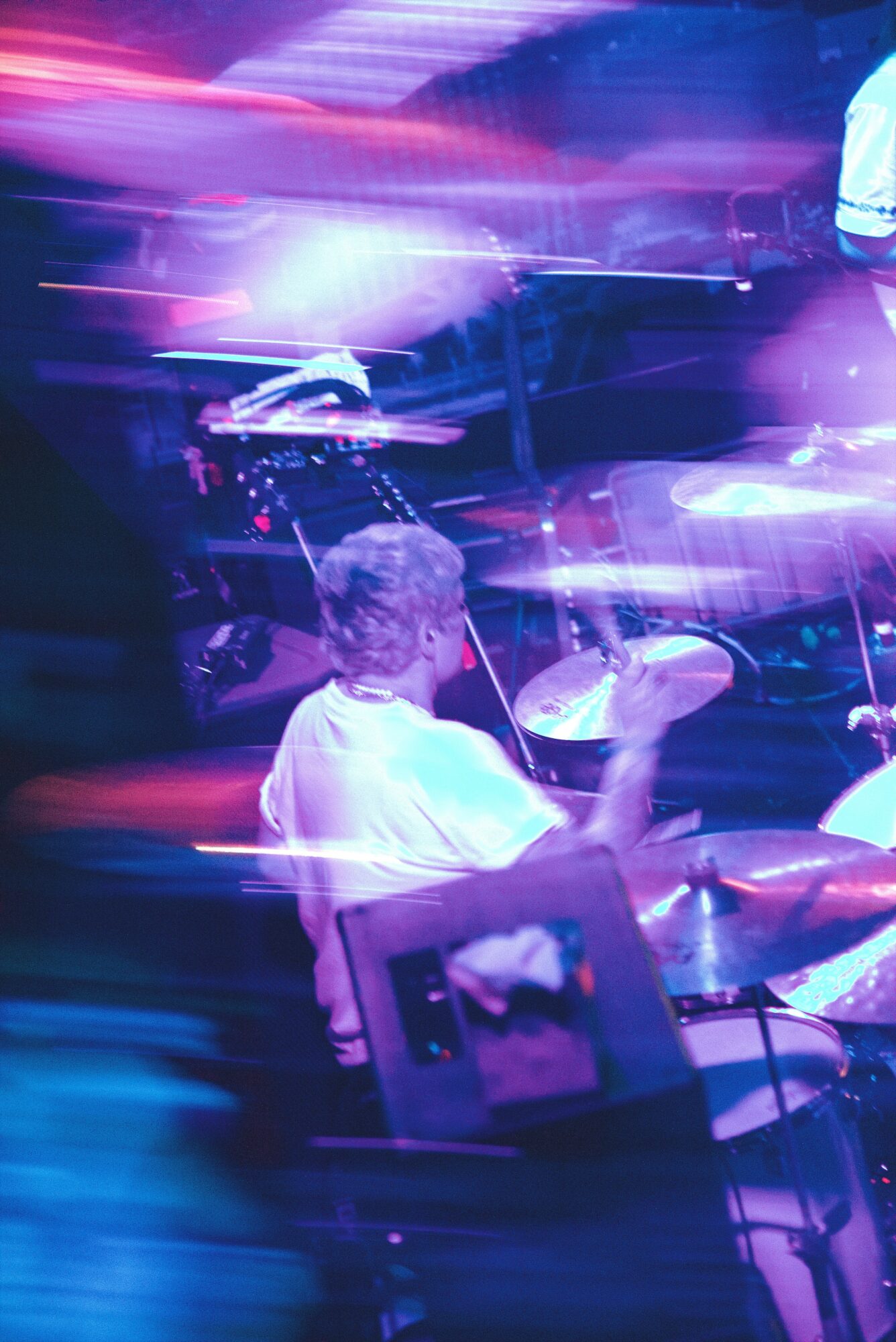 Person playing drums in a colorful, blurred concert setting with bright lights and motion effects.