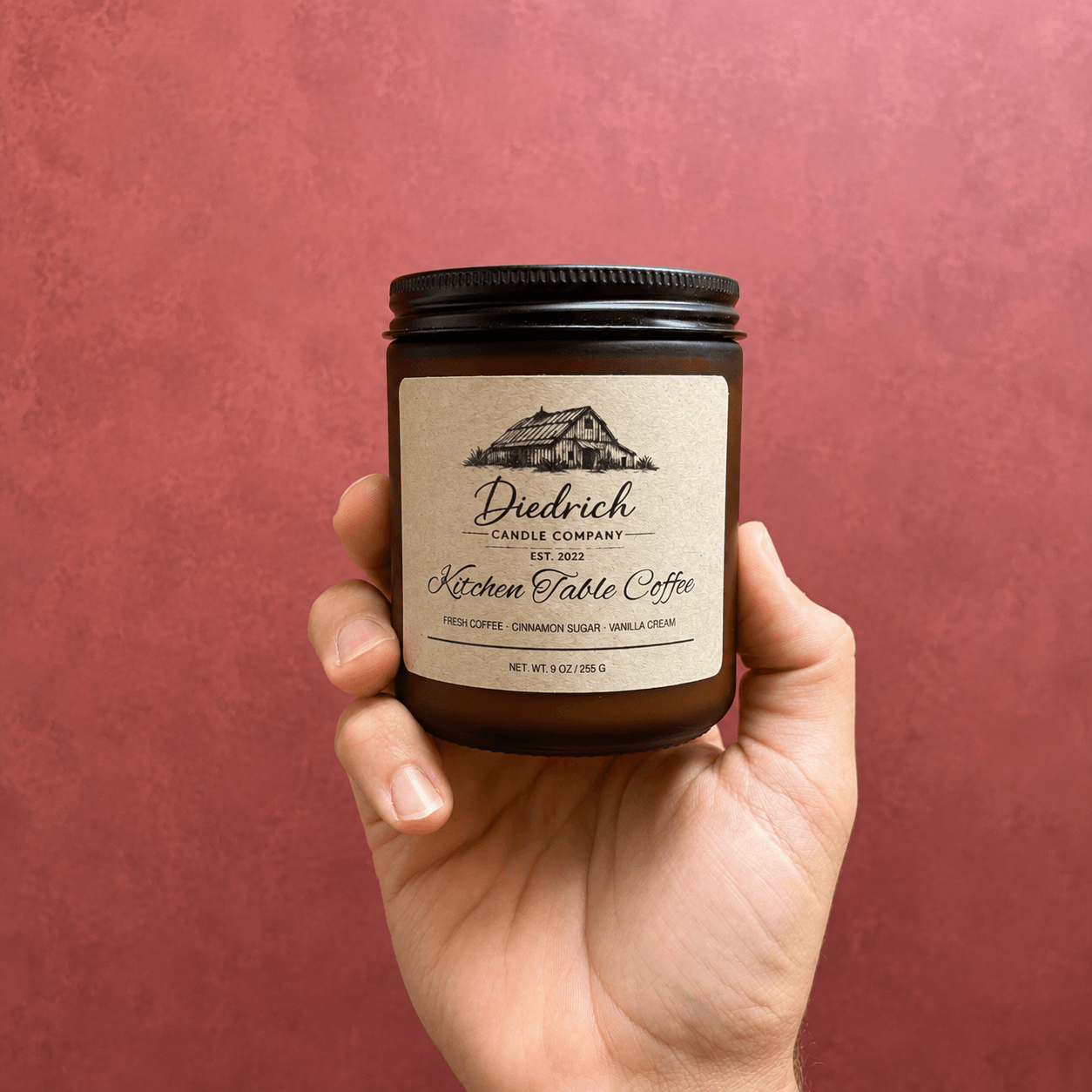 Hand holding a jar with a label reading 'Diedrich Kitchen Table Coffee' against a pink background.