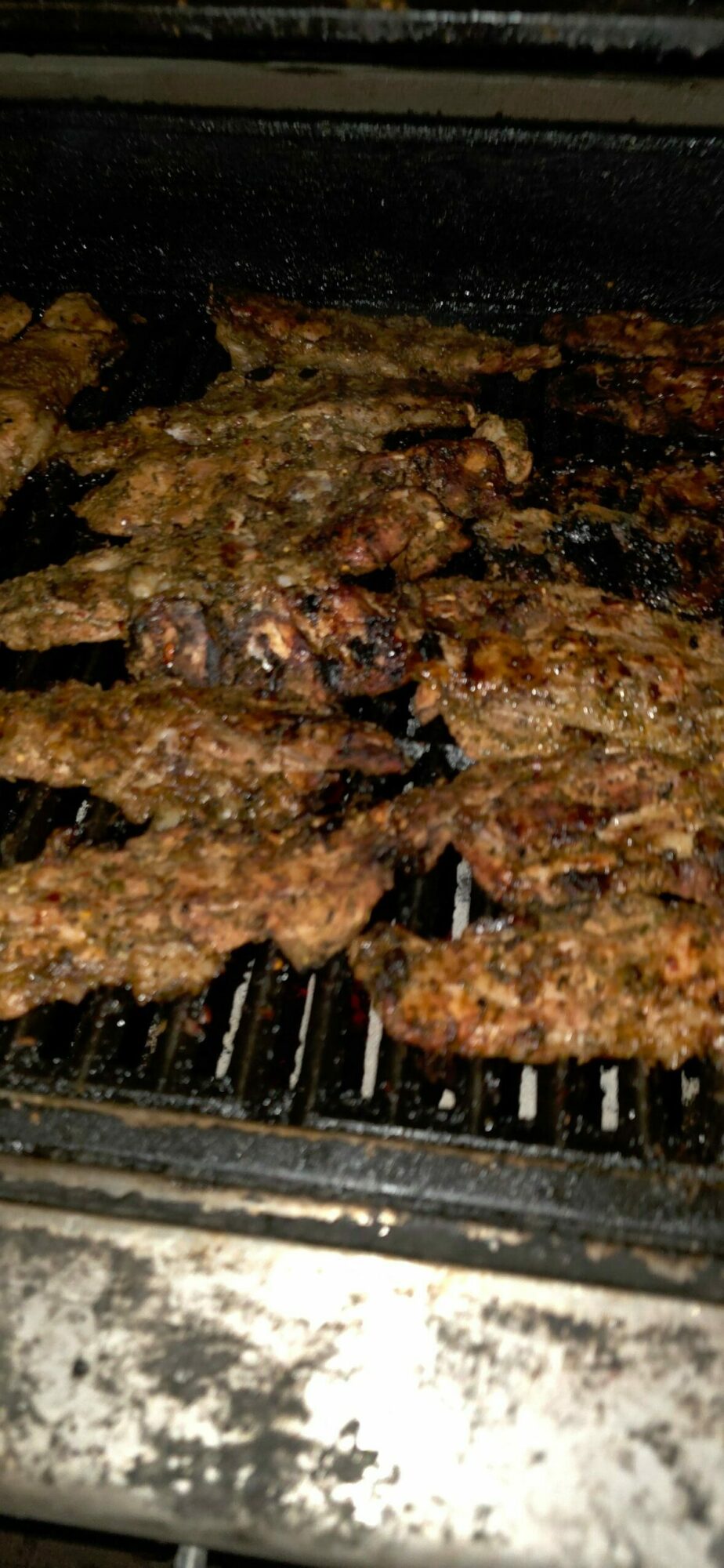 Grilled meat pieces on a grill with blackened surface, cooked to a brown color.
