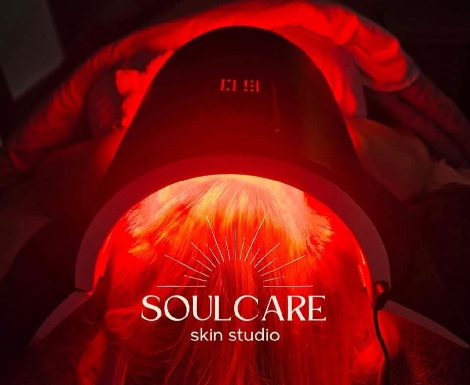Person receiving red light therapy in a skin studio, with a red glow and a device labeled SOULCARE skin studio.