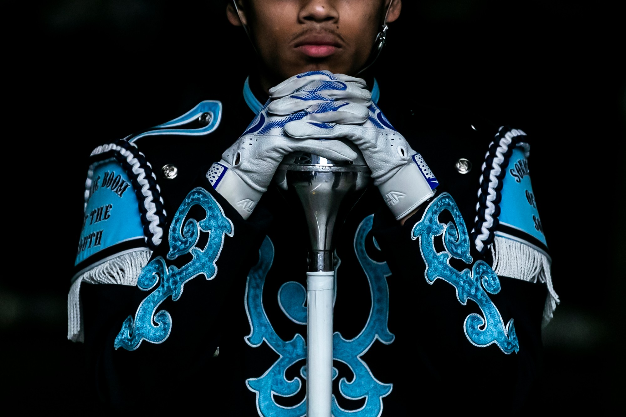 Person wearing ornate blue and black costume with gloves, holding a sword with both hands, dark background