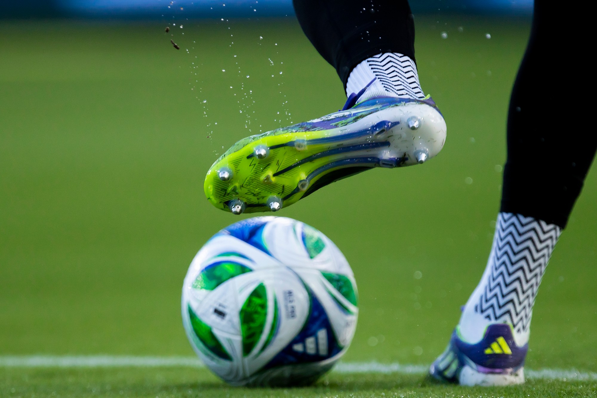 A soccer player kicks a ball on a field, wearing black and white shoes with patterned socks.