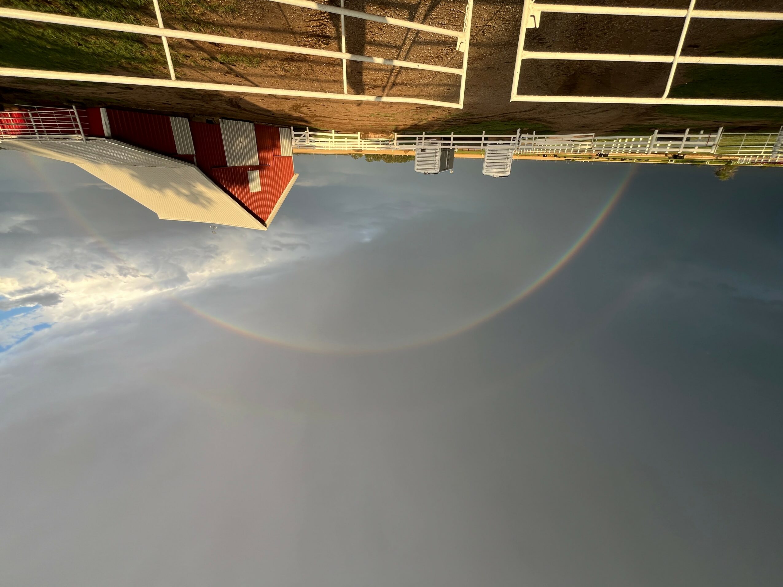 Cityscape with buildings and a rainbow in the sky, viewed from a rooftop or balcony, with a cloudy sky background.