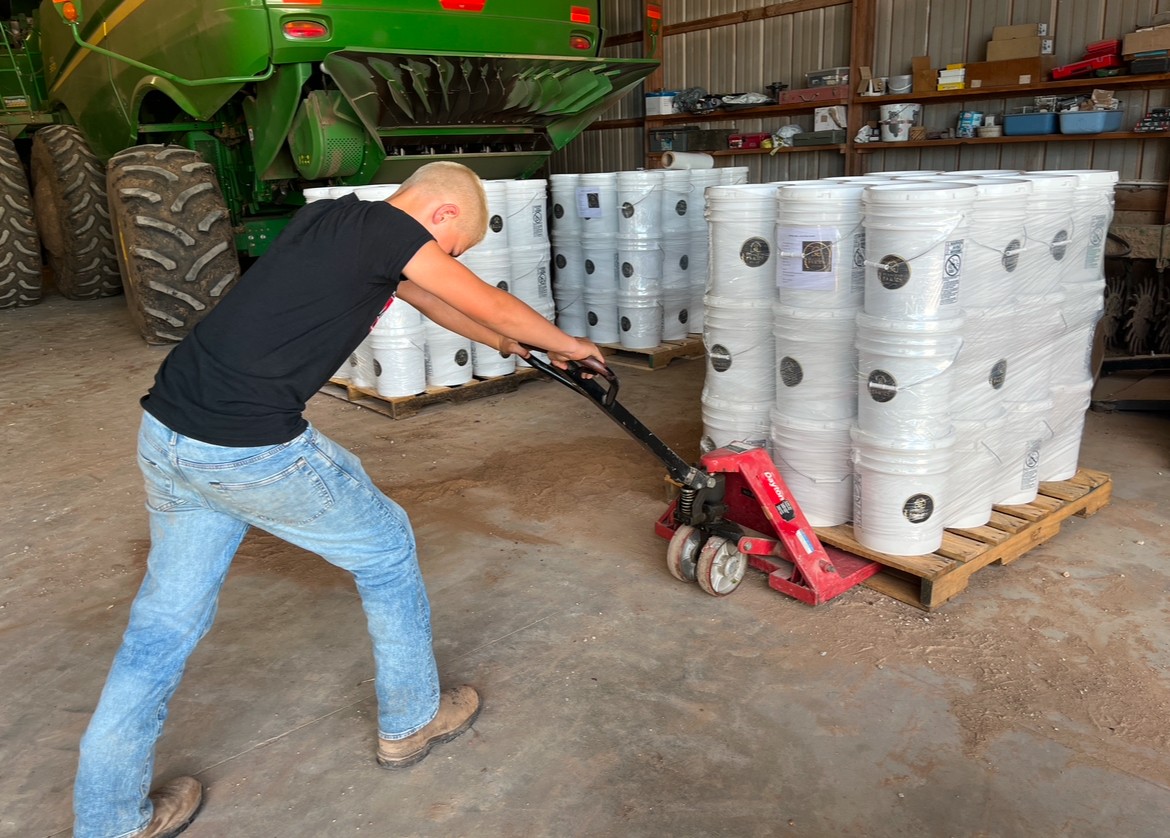 Person using a red floor roller on a concrete surface in a warehouse with stacked white rolls on a pallet