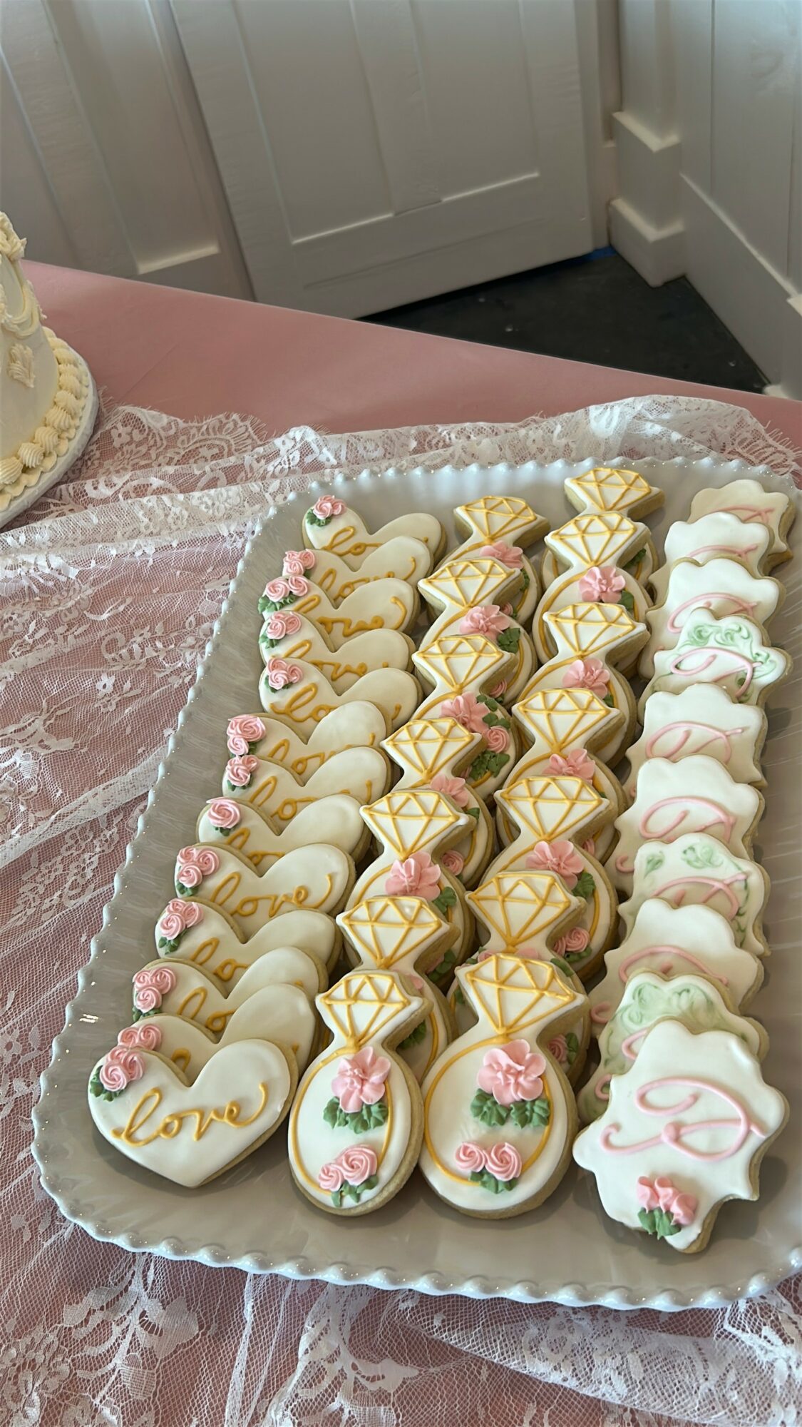 Tray of decorated cookies with floral and love-themed designs on a pink tablecloth.