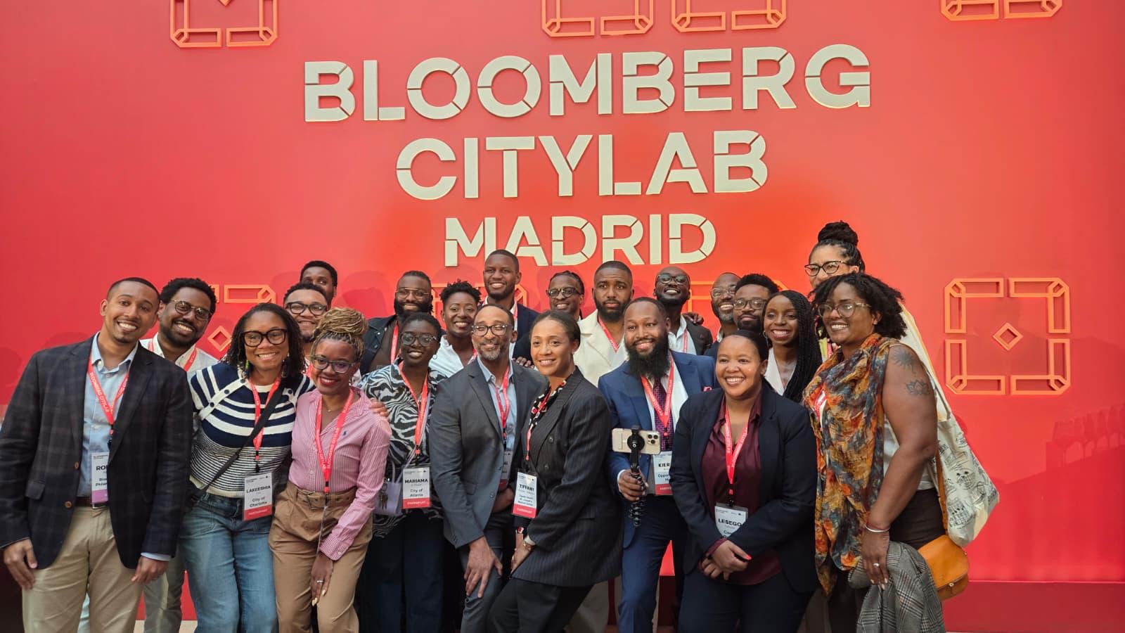 Group of people standing in front of a red backdrop with 'Bloomberg CityLab Madrid' text, smiling and posing for a photo.