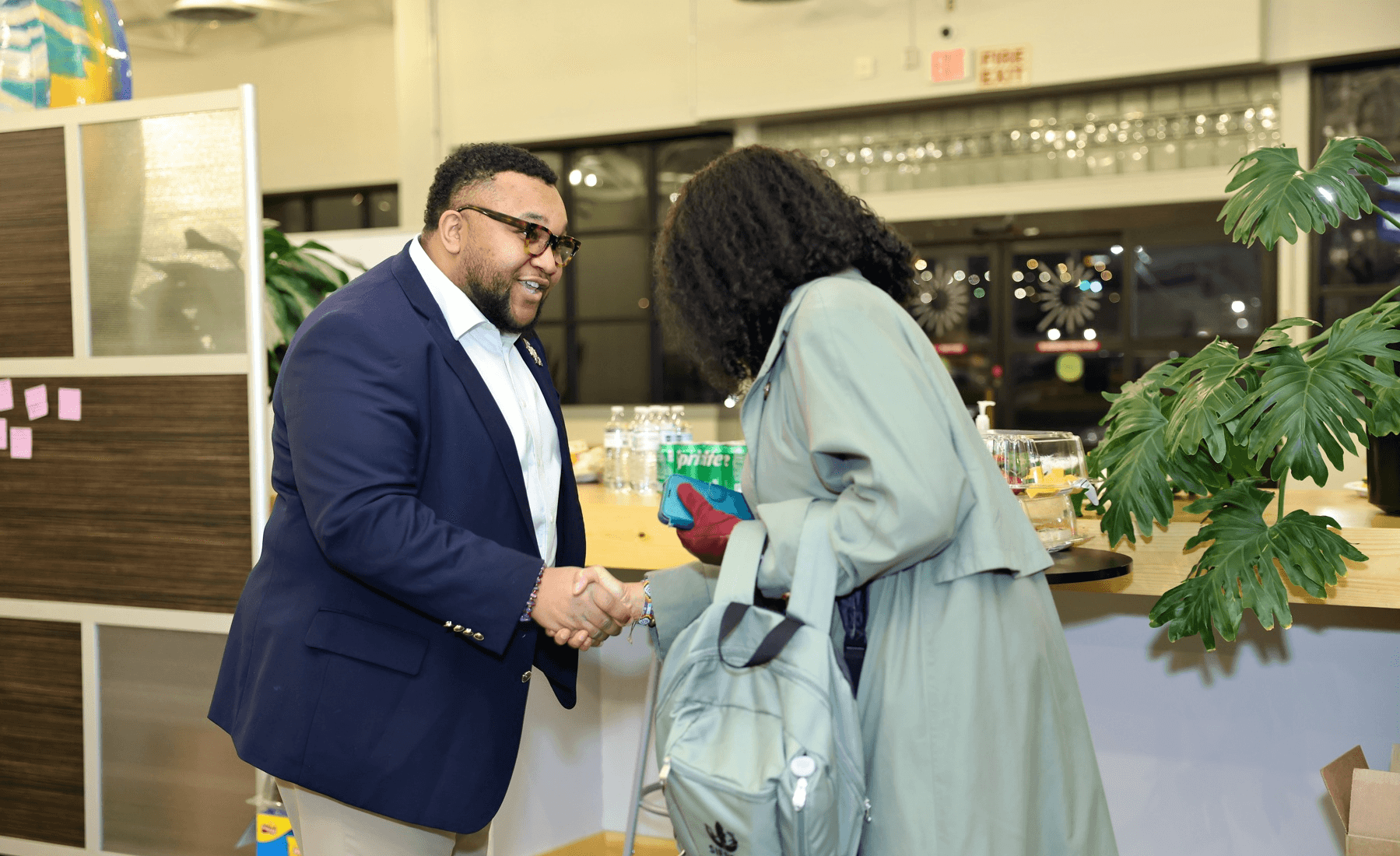 Two people shaking hands in a modern indoor setting with plants and a bar in the background.