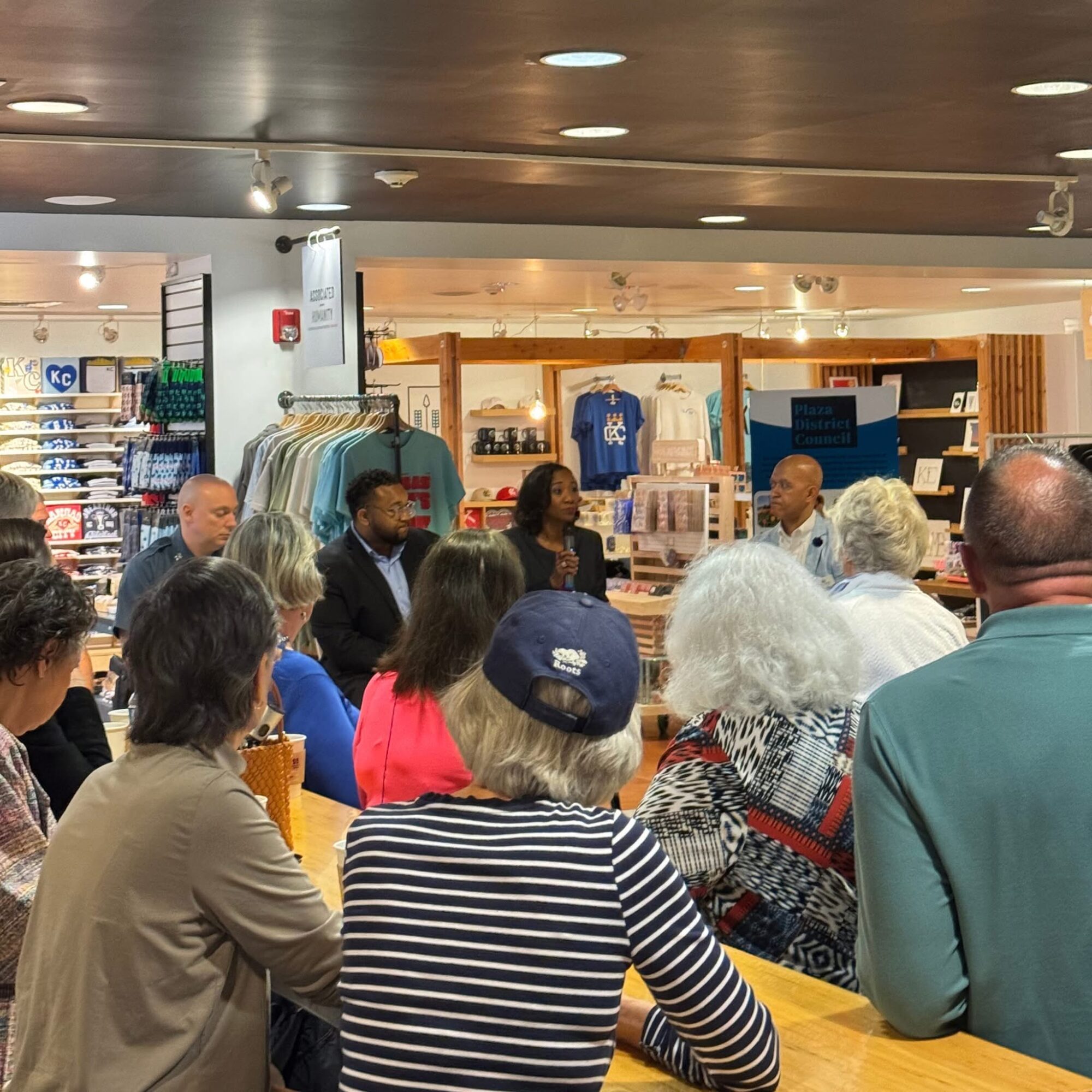 Group of people gathered around a speaker in a retail store, with clothing and merchandise in the background.