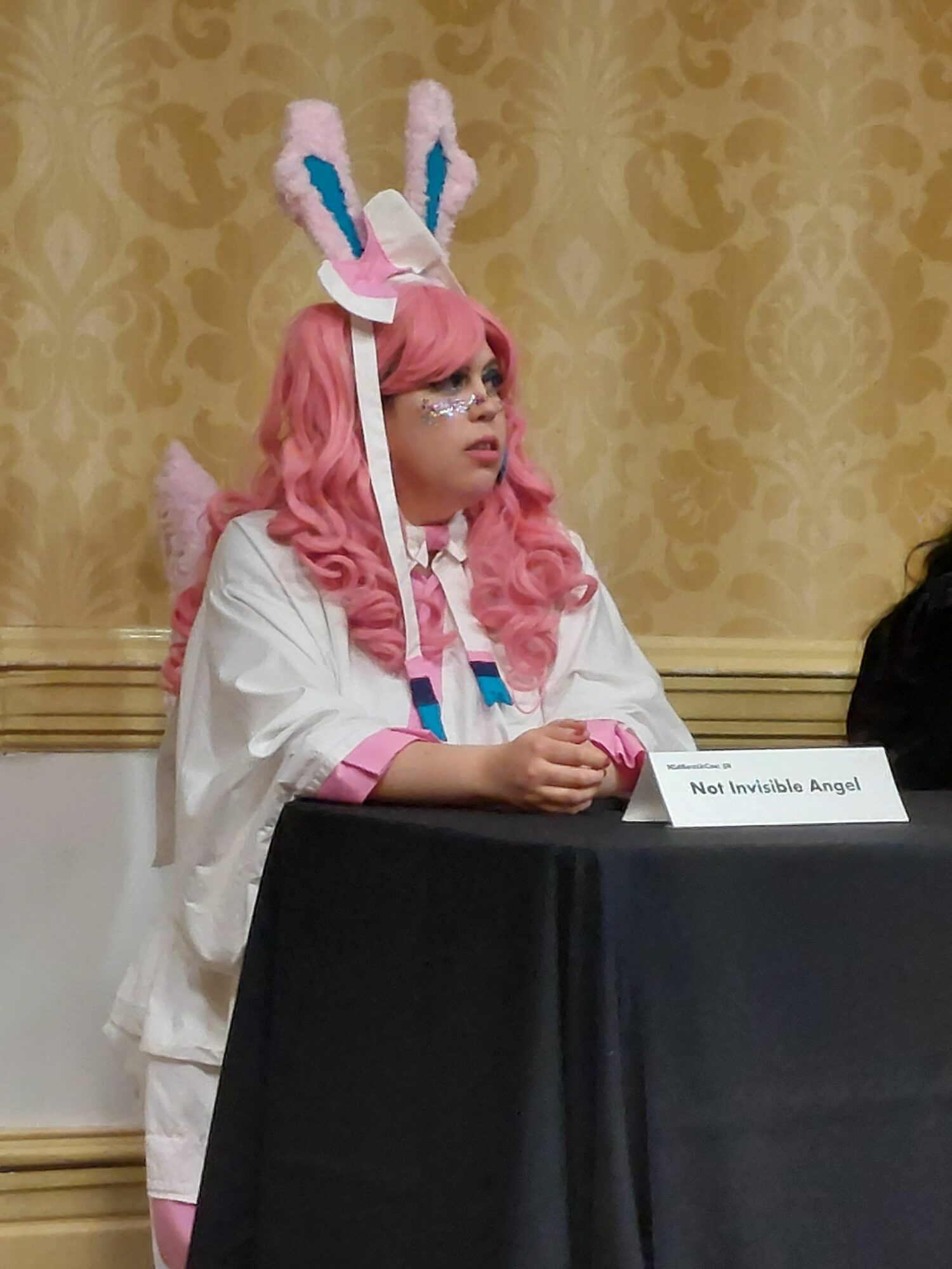 Child dressed as a pink and white unicorn with a horn and ears, sitting at a table with a black tablecloth.