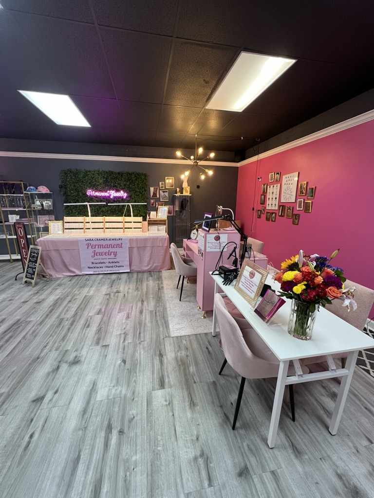 Indoor event space with pink and white decor, tables with jewelry displays, and a pink wall with framed pictures.
