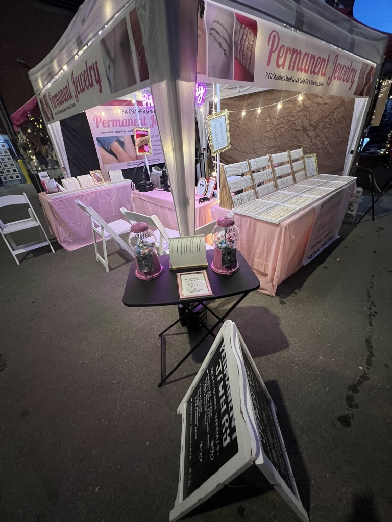 Nighttime outdoor booth with pink and white decor, seating area, and promotional banners for permanent makeup.