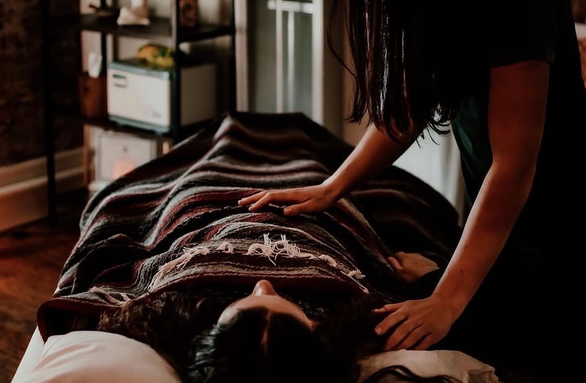 Person receiving massage on a bed, with a massage therapist applying pressure on their back, in a cozy room.