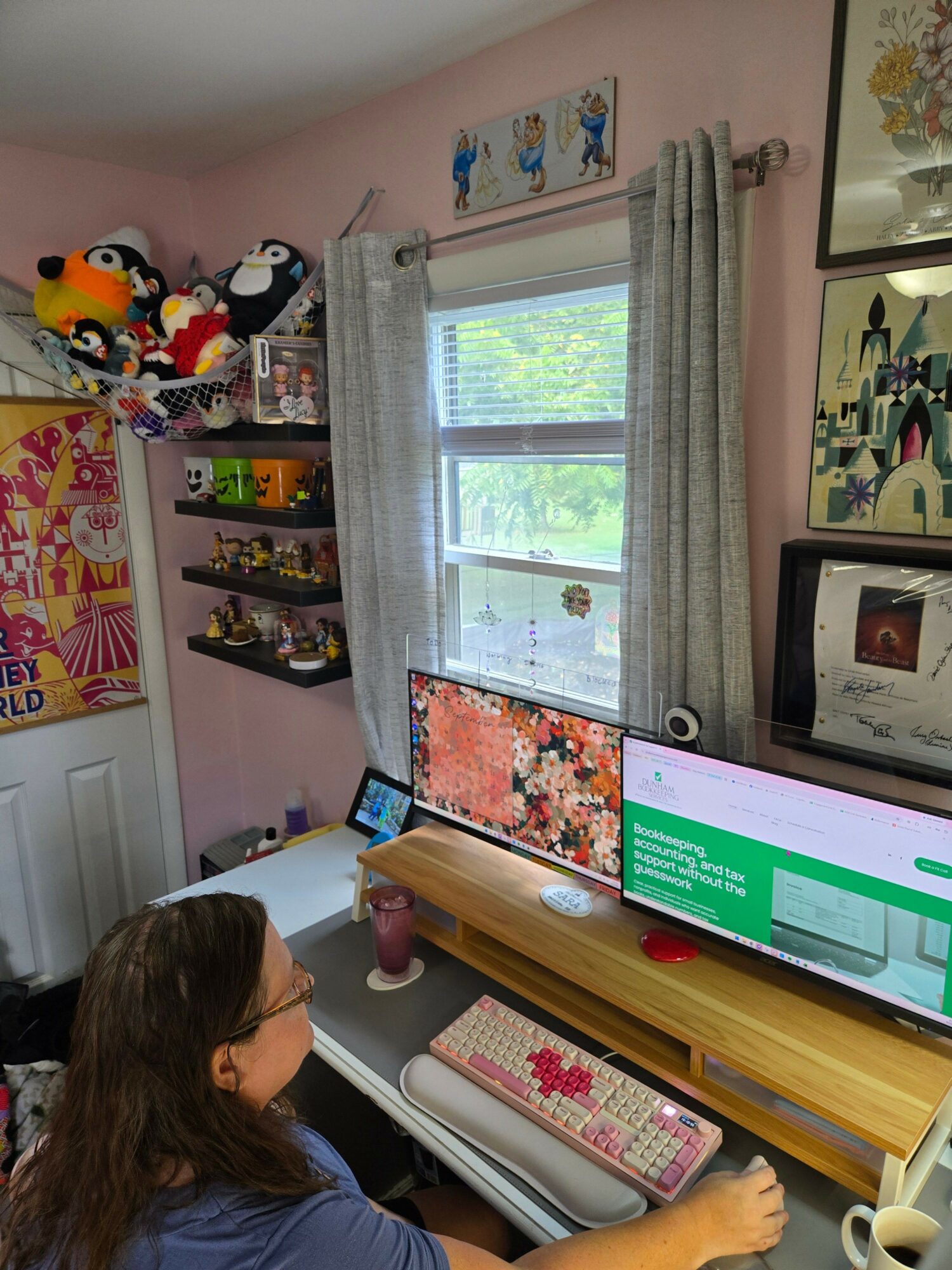 Child with long hair looking at a computer monitor in a pink room with shelves and window.