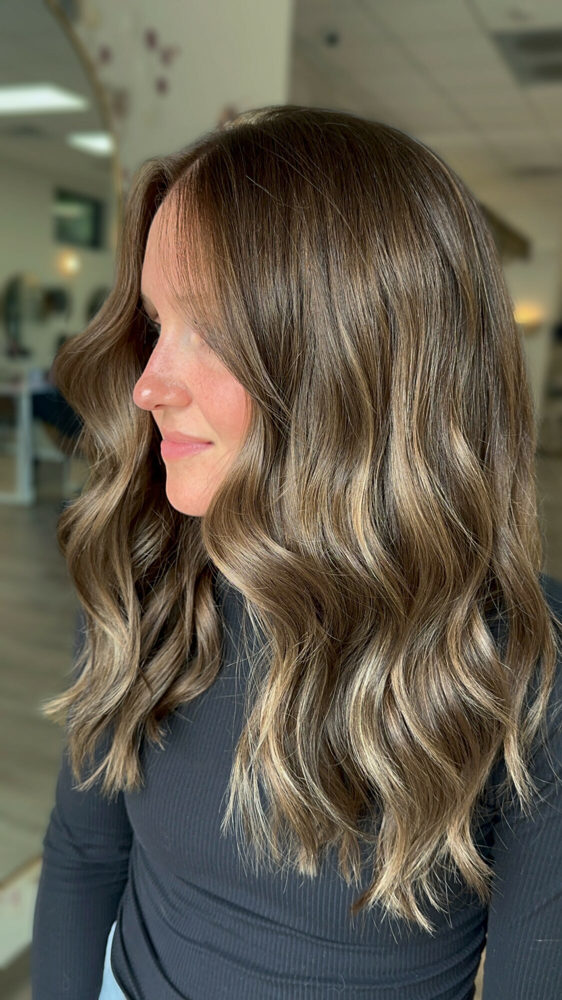 Side view of a woman with long, wavy, light brown hair in an indoor setting.